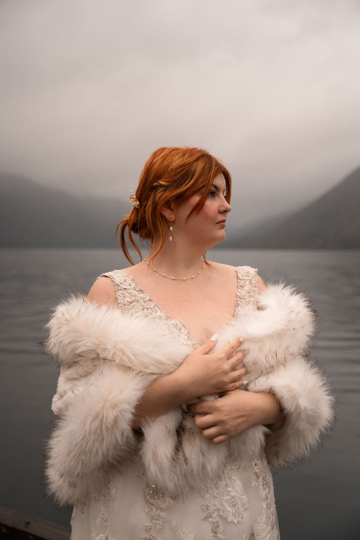 Dramatic lakeside portraits with person wearing white fur wrap against misty mountain backdrop.