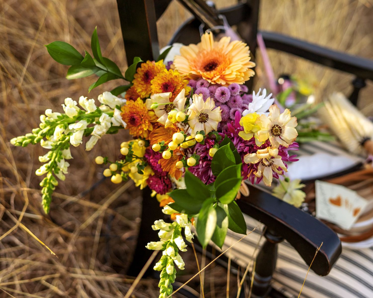 Colorful wildflower arrangement on wooden chair outdoors.