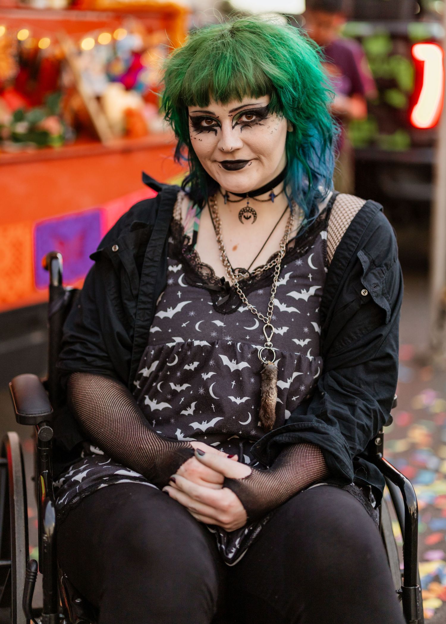Alternative fashion enthusiast in black attire with green hair sitting in a casual pose.