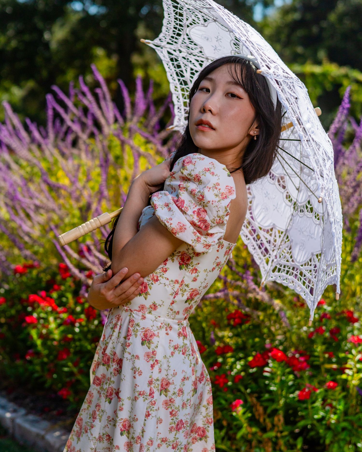 Elegant garden portrait with white lace parasol and floral dress against vibrant purple flowers.