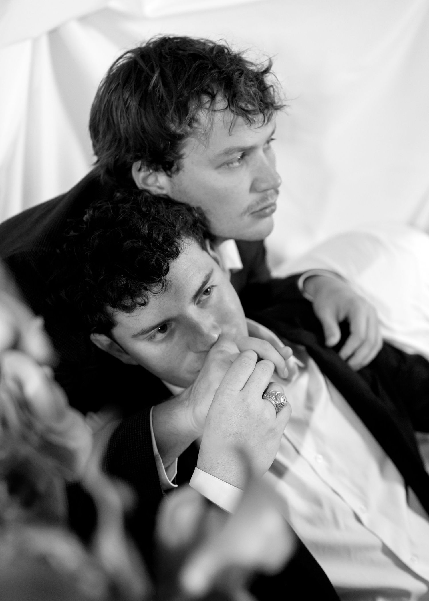 Black and white photo of two young men in suits, one resting his head on the other's shoulder at a formal event.