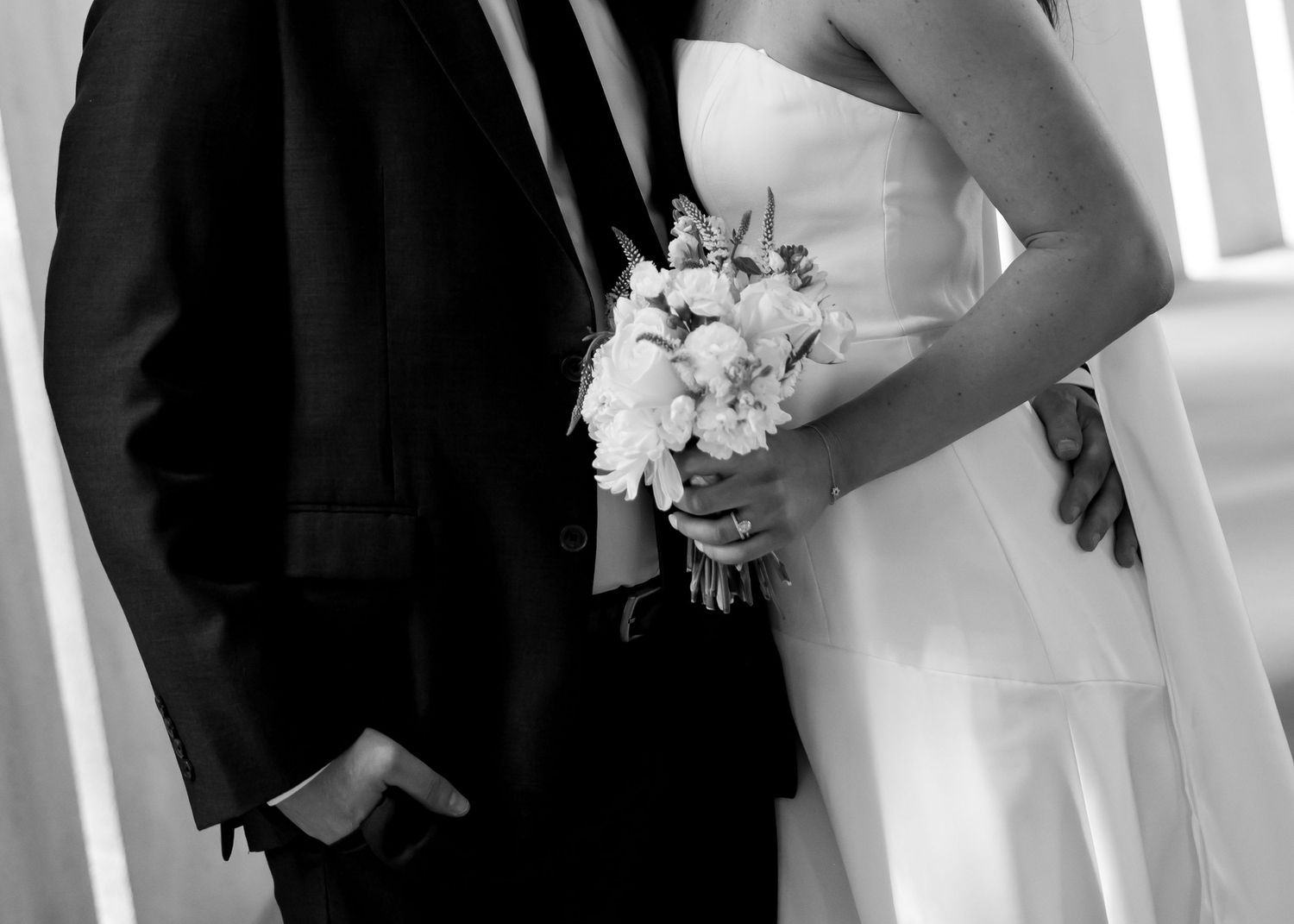 Black and white photo of bride and groom holding floral bouquet at wedding ceremony.