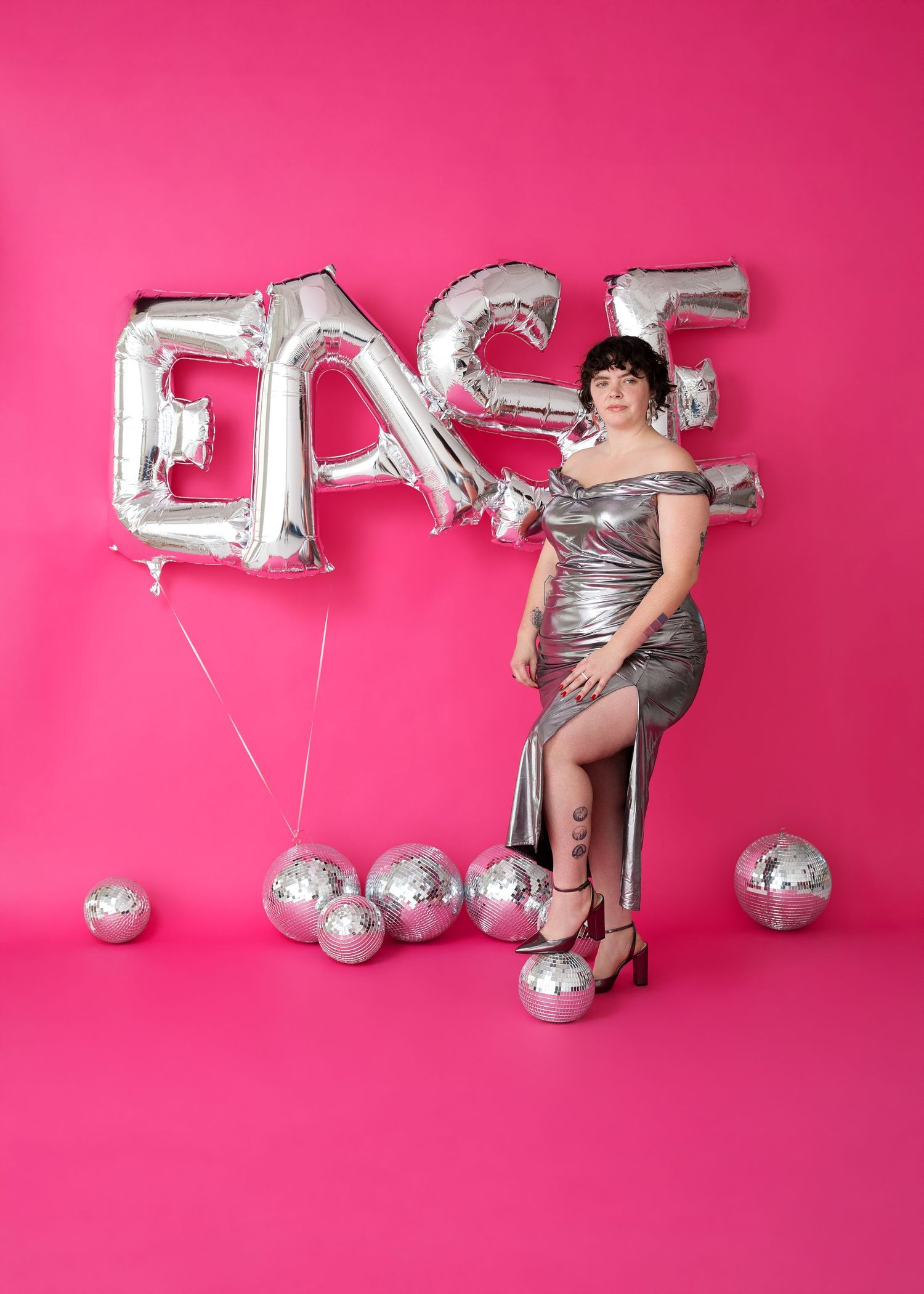 Silver balloon letters and disco balls arranged on bright pink backdrop for festive party setup.
