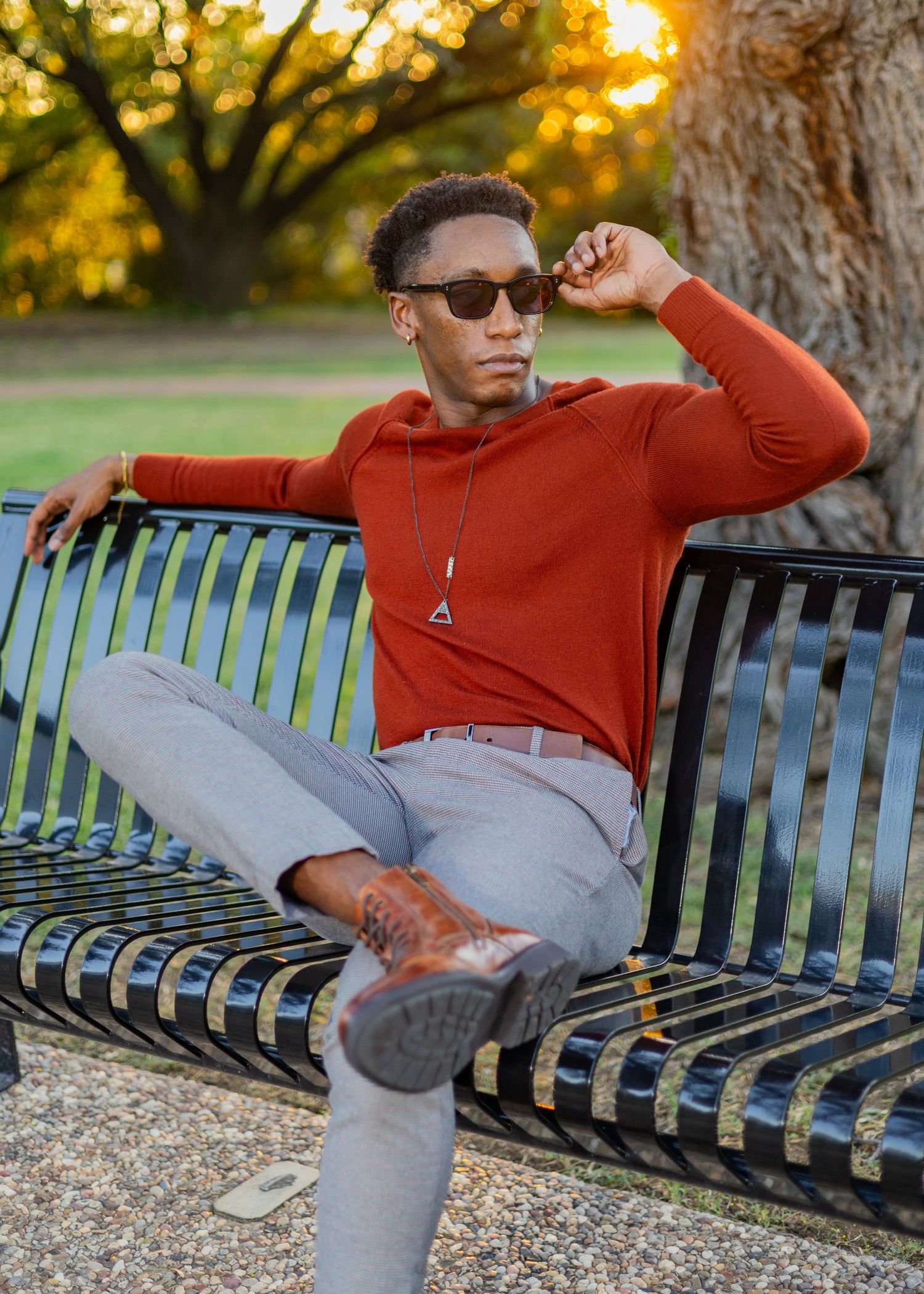 A casual outdoor scene shows someone relaxing on a park bench in a red sweater and gray pants.