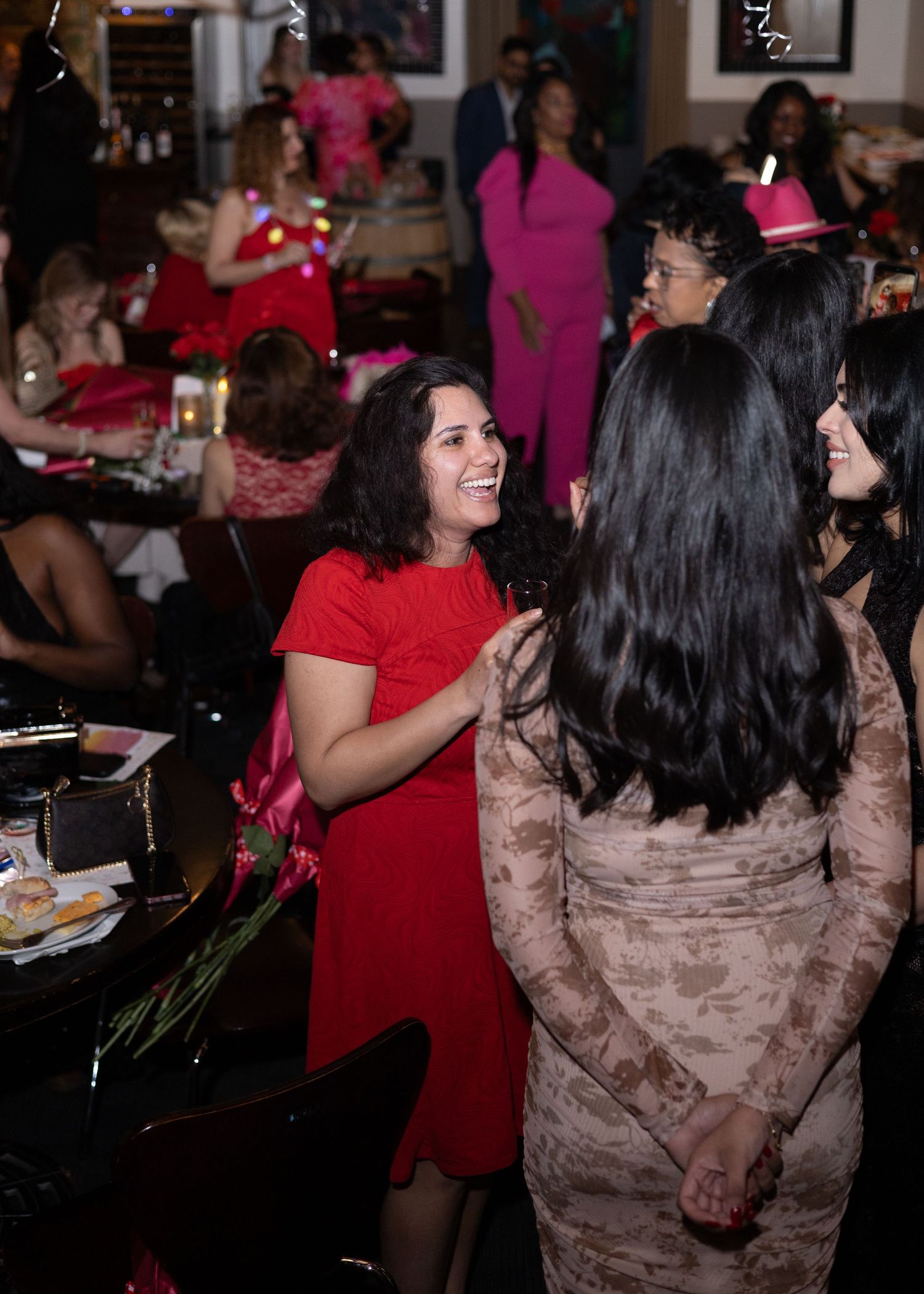 People in red and pink outfits dancing and socializing at an indoor event with dark lighting.