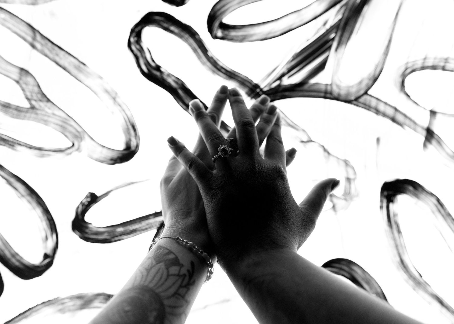 Two hands pressed together against abstract black brushstroke art in a striking black and white photograph.