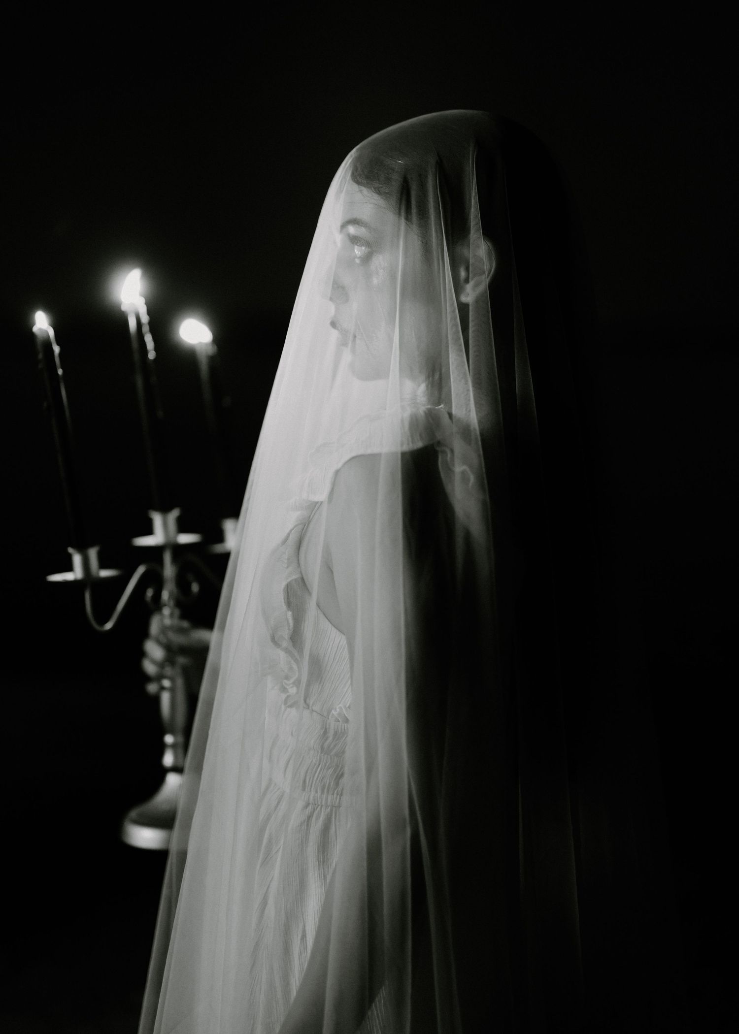 Dramatic black and white photo of veiled figure with candelabra in background.