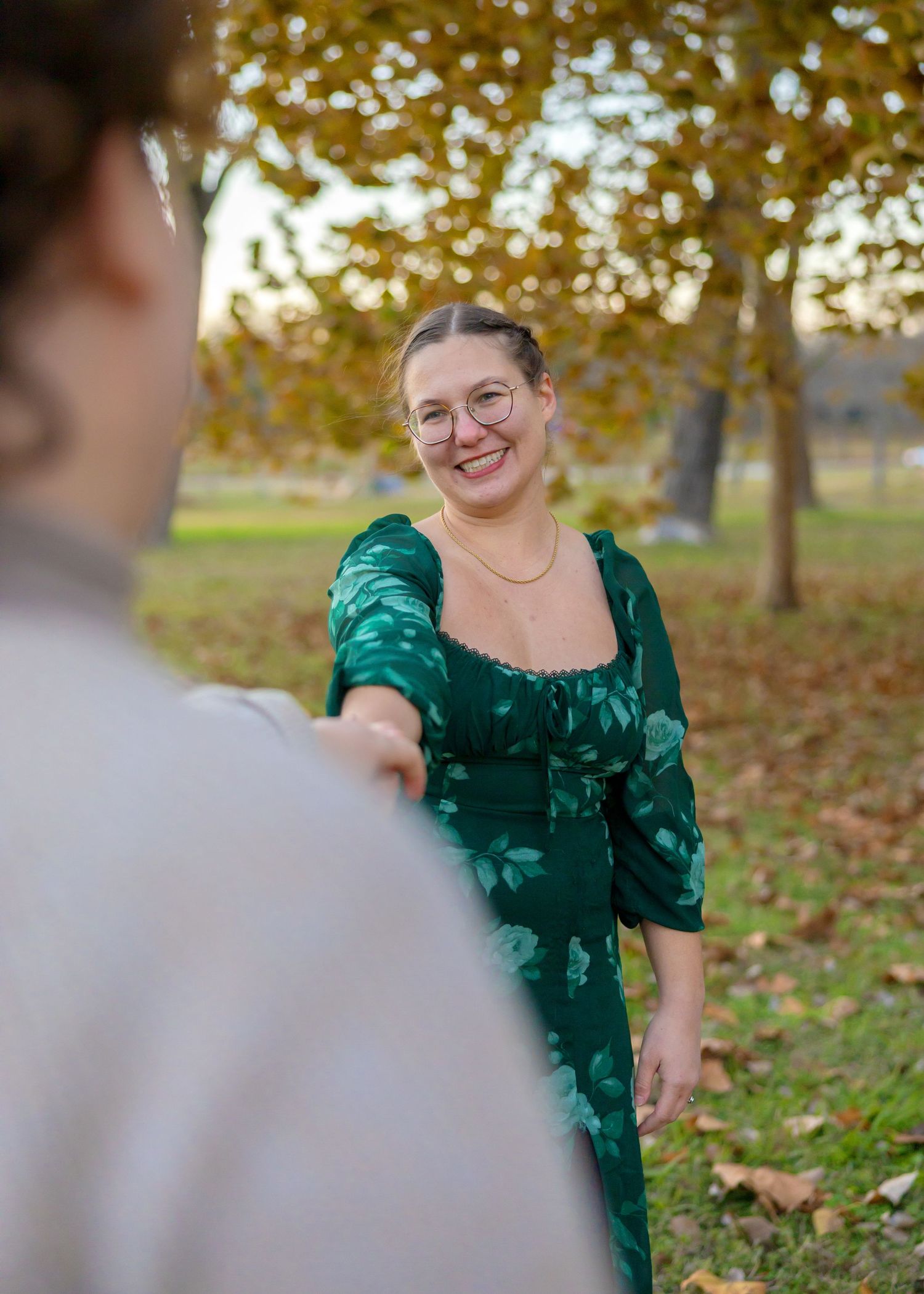 Person in emerald green dress smiling and reaching out during an autumn photoshoot.
