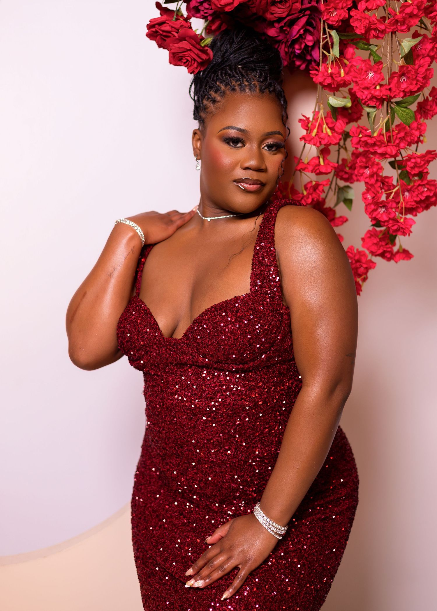 A stunning burgundy sequin gown is showcased in an elegant photoshoot with vibrant red floral accents.