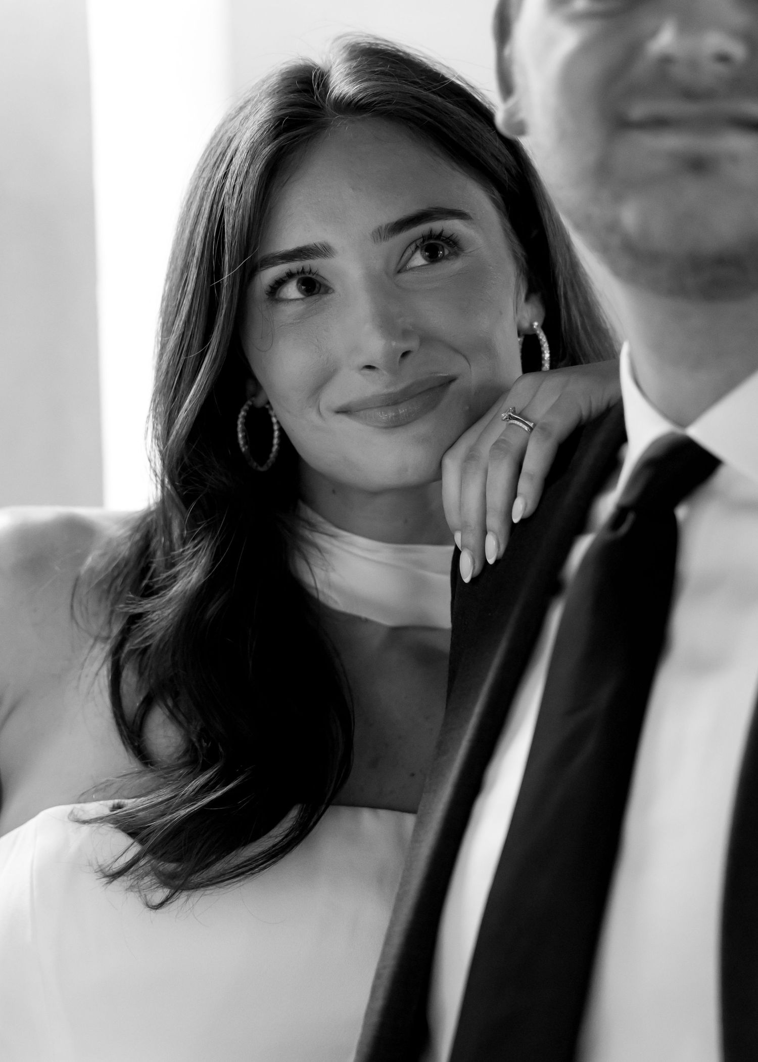 Black and white photo of a smiling young woman in a white dress leaning on a man in a suit and tie.