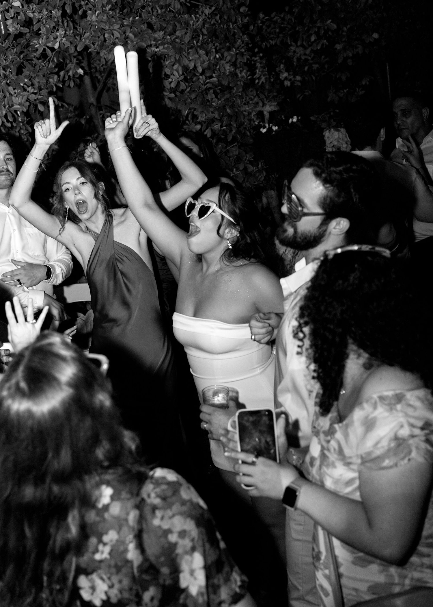 Black and white photo of joyful wedding guests dancing and celebrating at a lively outdoor reception party.
