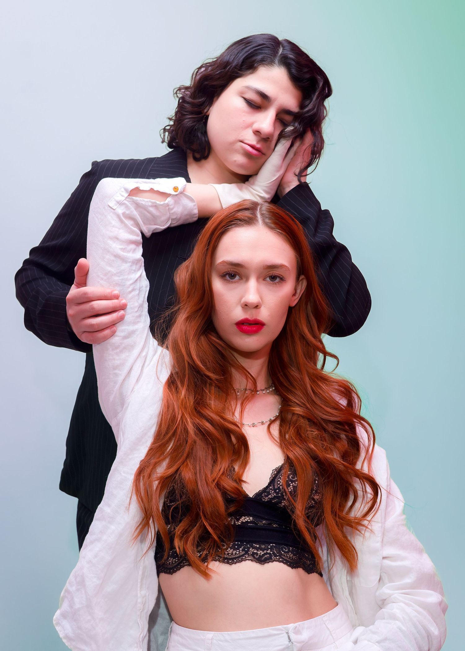 Artistic fashion photoshoot with two models in black and white clothing against turquoise background.