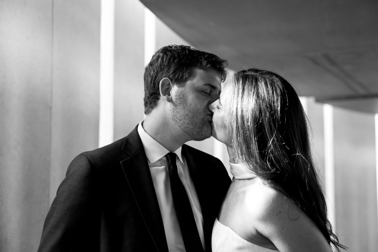 Black and white photo of a couple sharing a romantic kiss, man in suit and tie, woman in elegant dress.