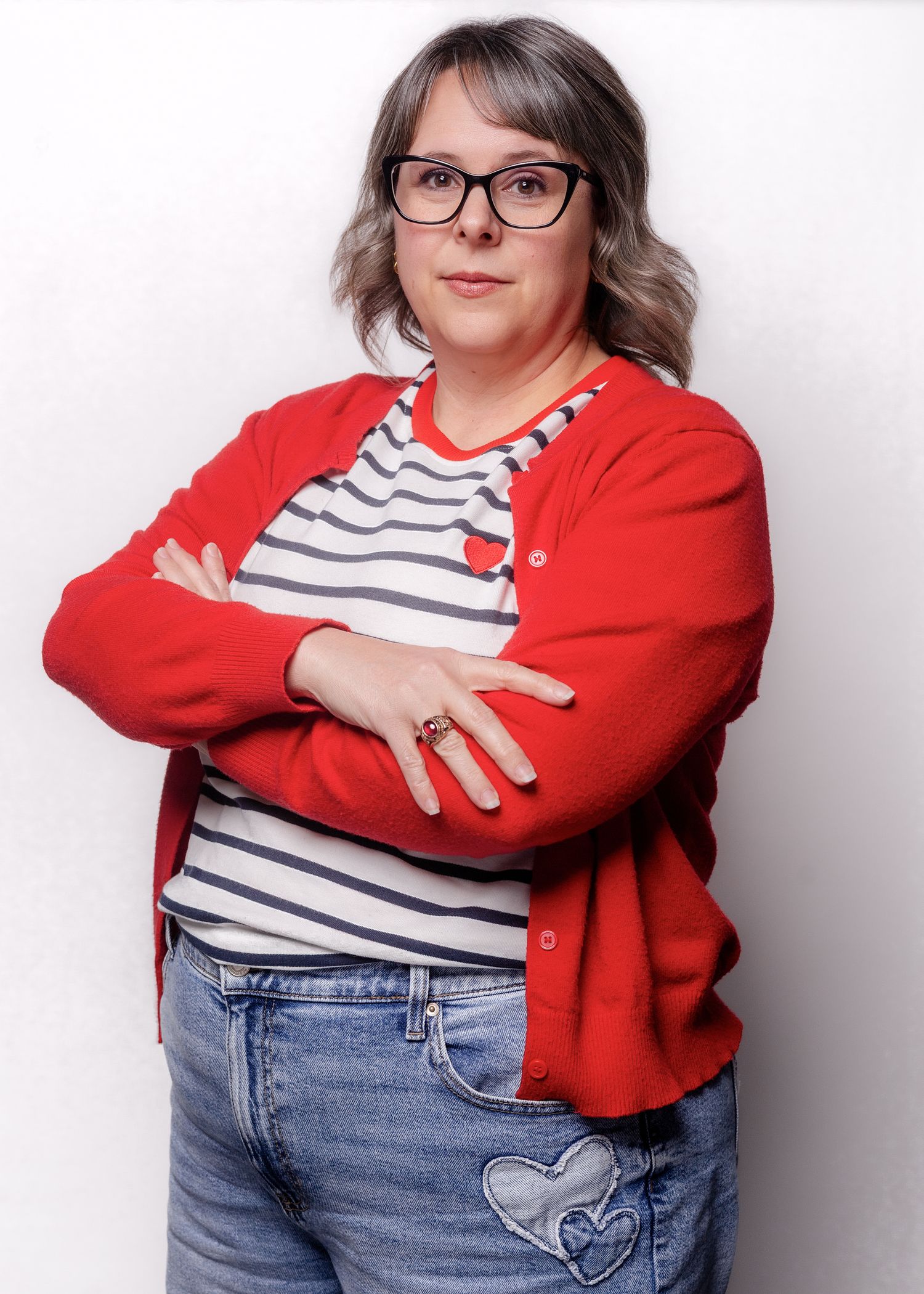 Person wearing red cardigan and striped shirt poses against white wall showing embellished jeans.