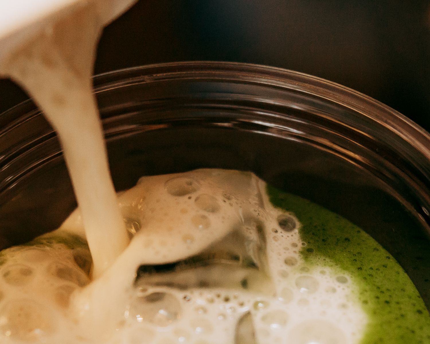 Close-up of green matcha tea being poured into a glass with frothy bubbles.