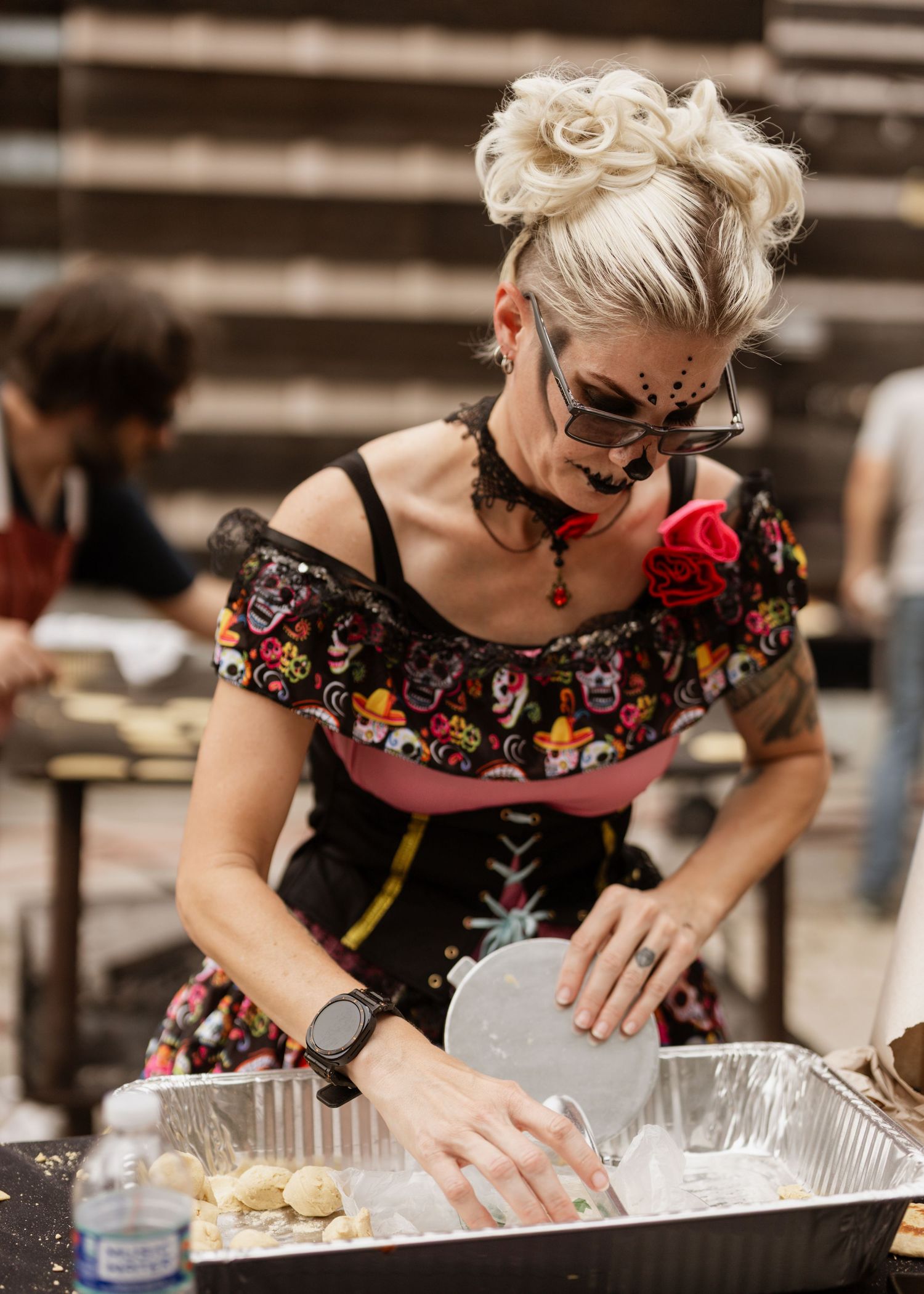 A person in a floral dress and face paint prepares food at an outdoor festival or event.