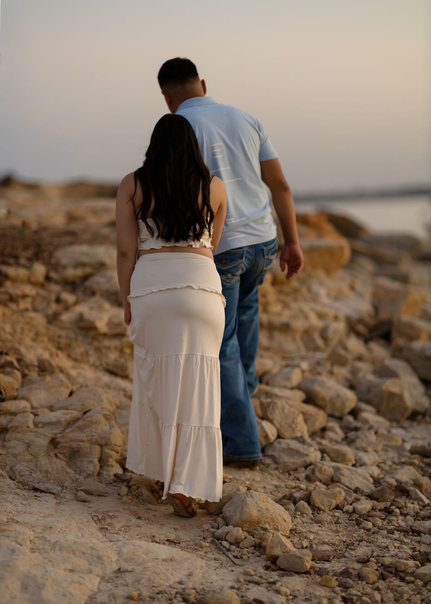 Couple walks along rocky coastal shoreline during evening light.