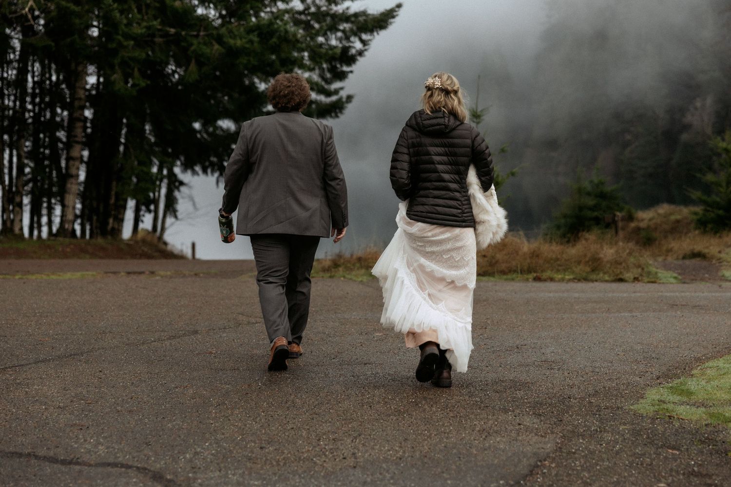 Bride and groom walking away together on a misty road surrounded by trees after their wedding.