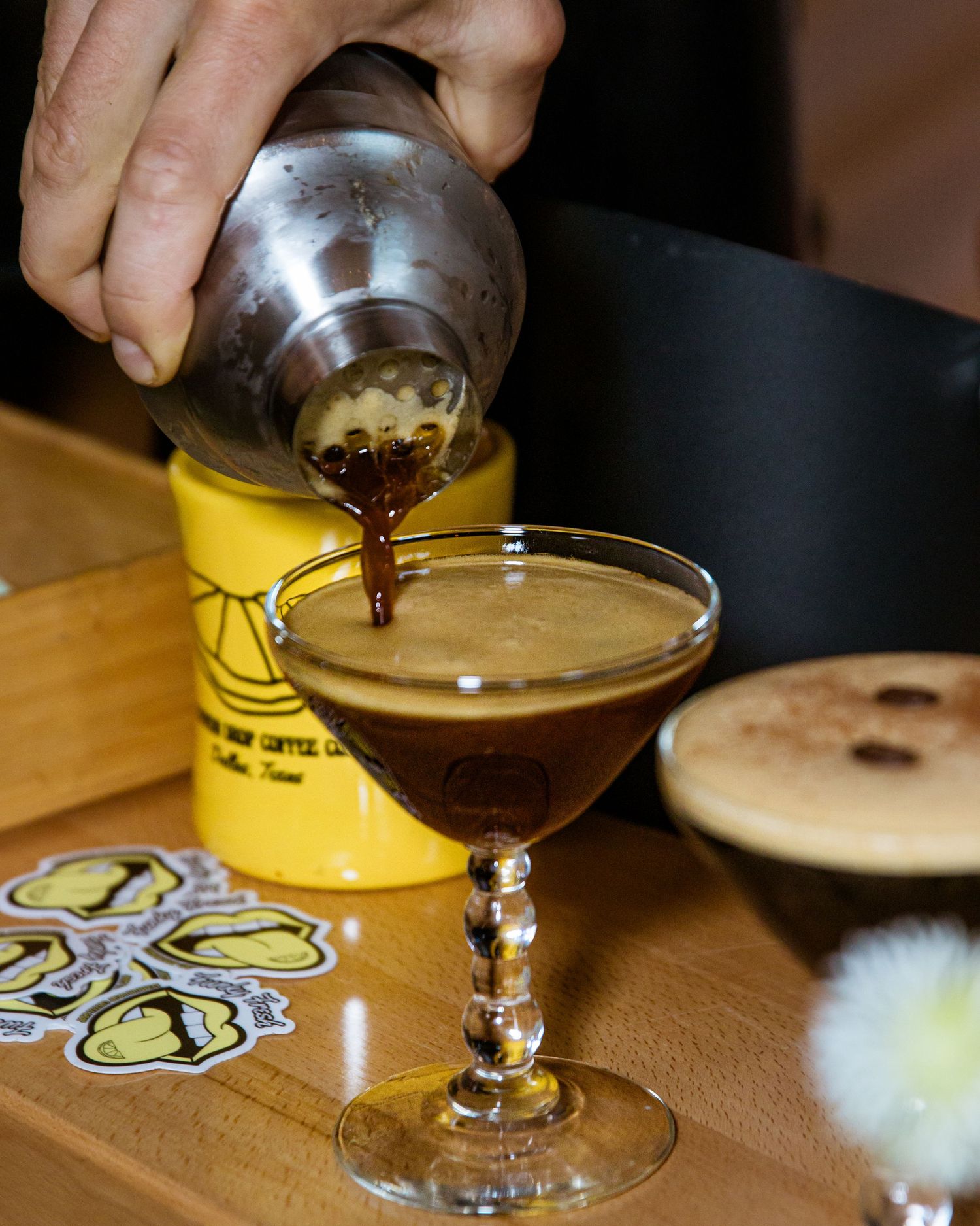 Cocktail being poured into an elegant coupe glass at a bar.