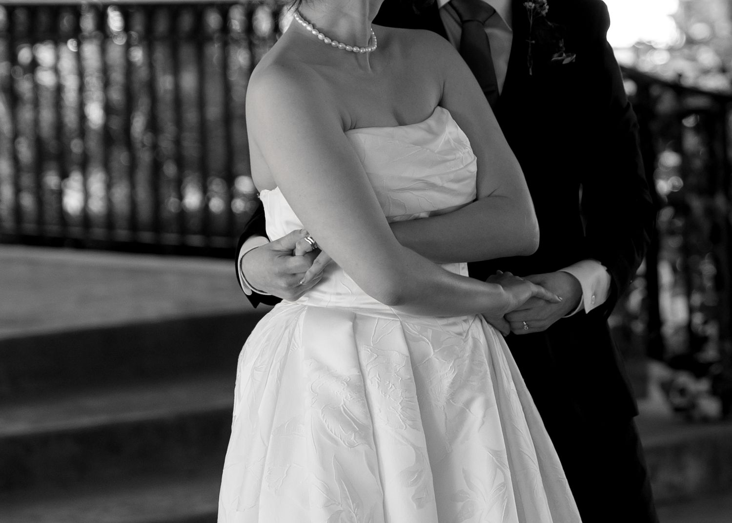 Black and white photo of a bride in a strapless gown and groom in a suit embracing at a wedding.