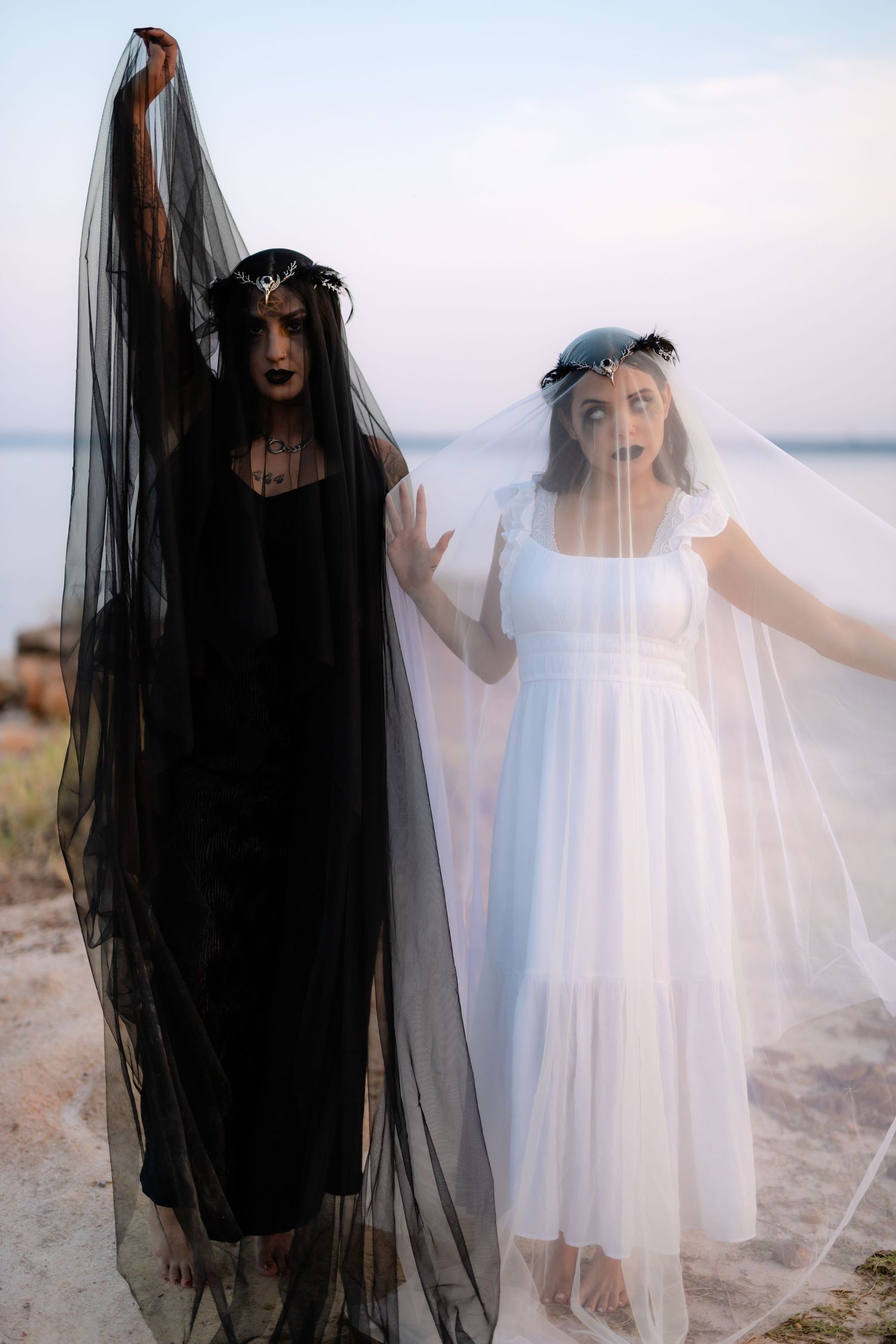 Two ethereal figures in contrasting black and white dresses with long veils pose dramatically against a misty landscape.