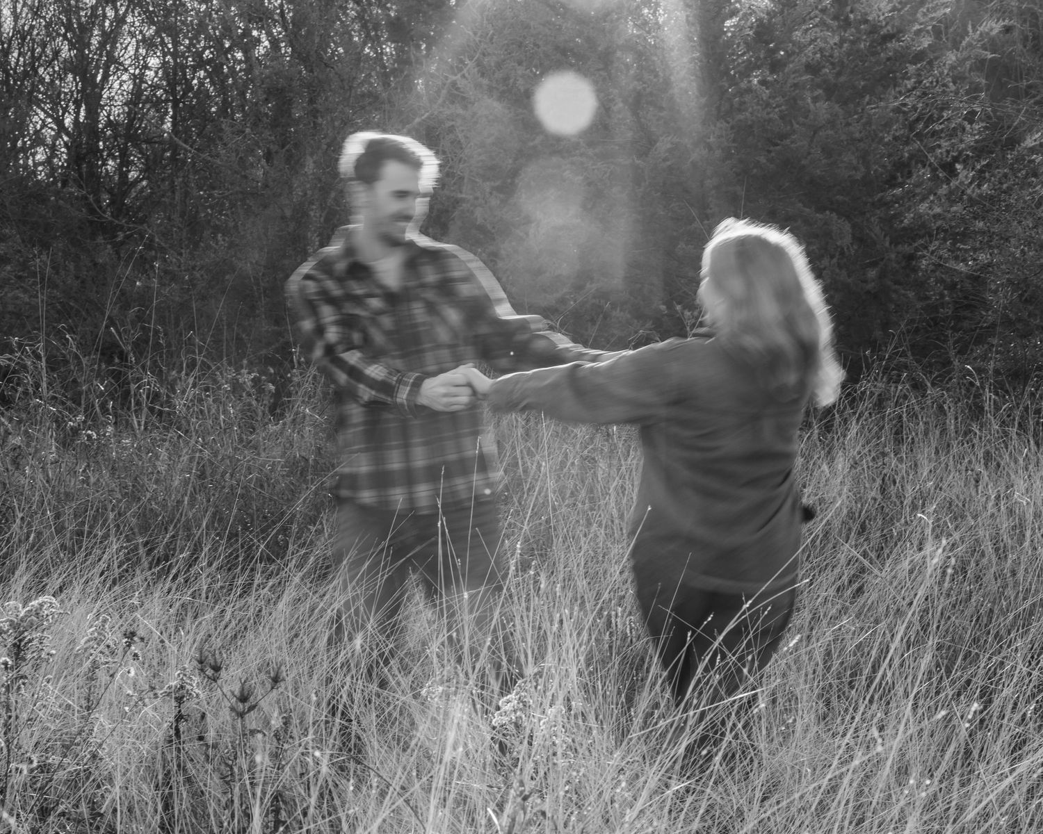 Blurred black and white image of two people moving through tall grass.
