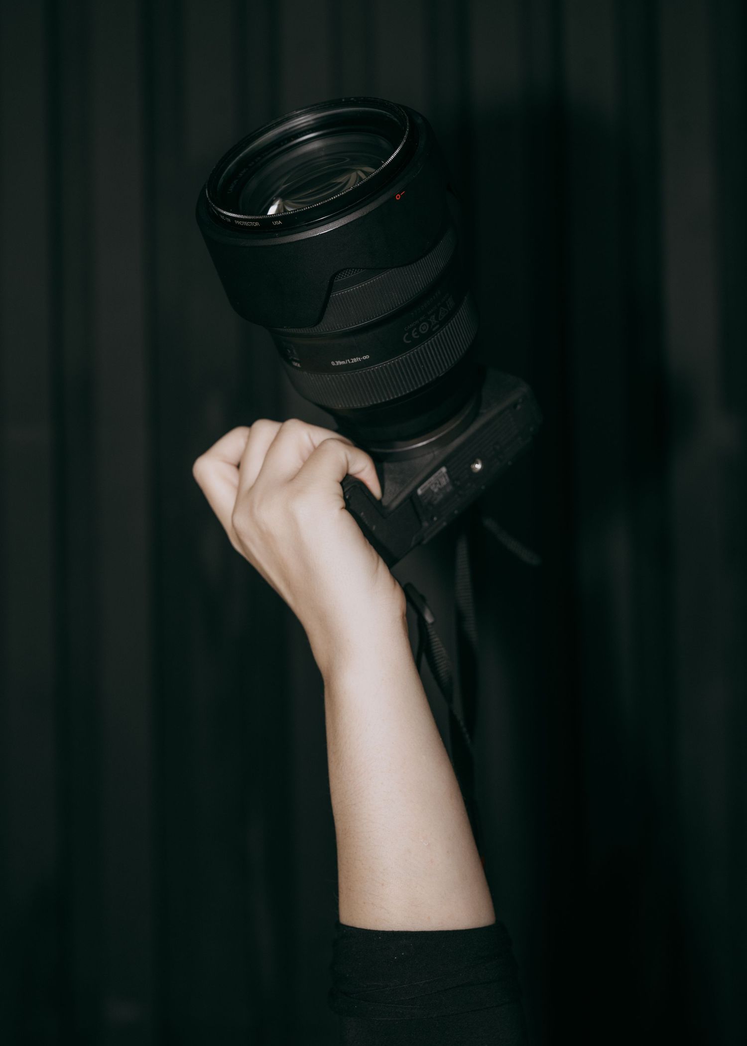 Hand holding a black leather belt against a dark background in dramatic lighting.