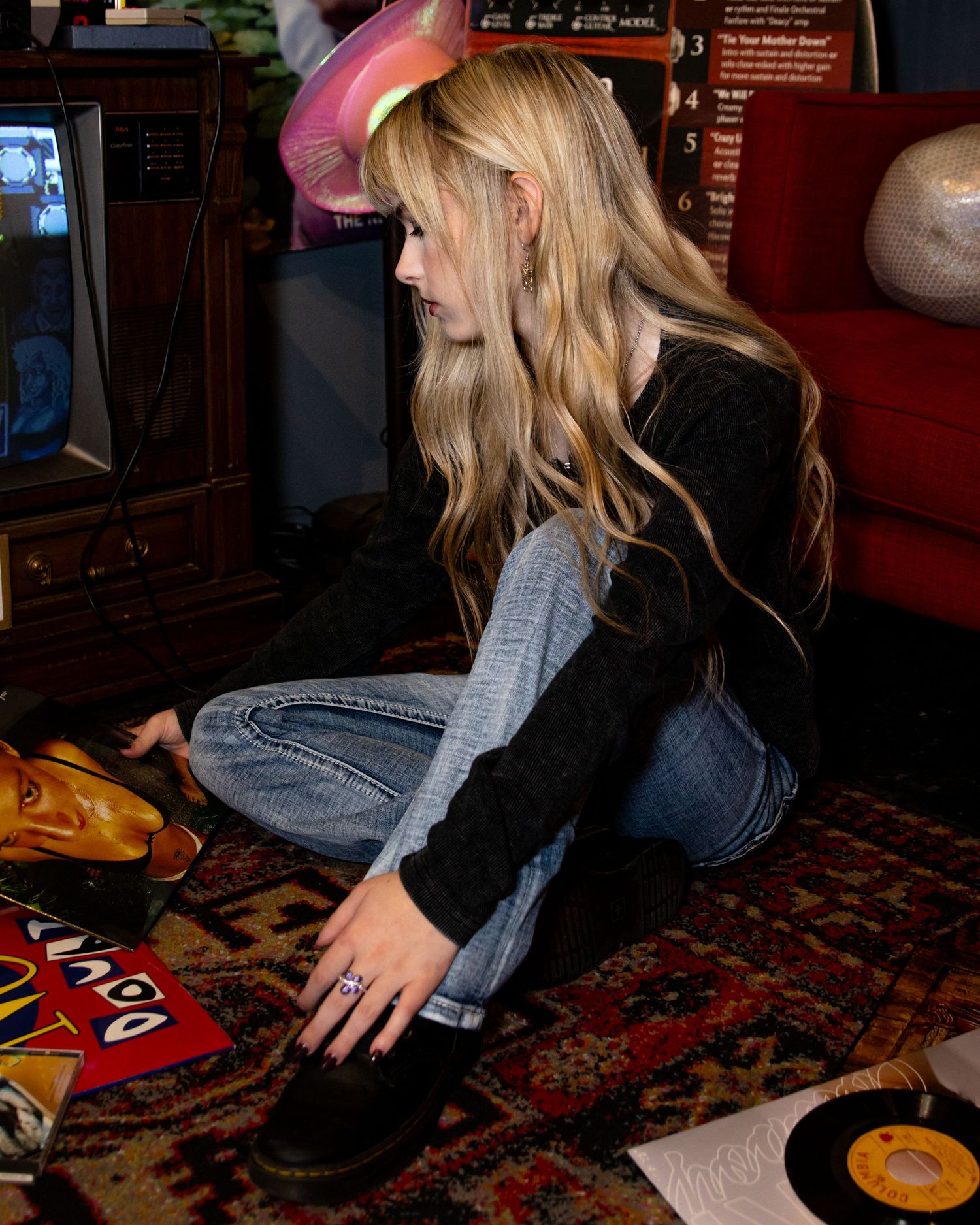 Person looking through vinyl records while sitting on patterned carpet.