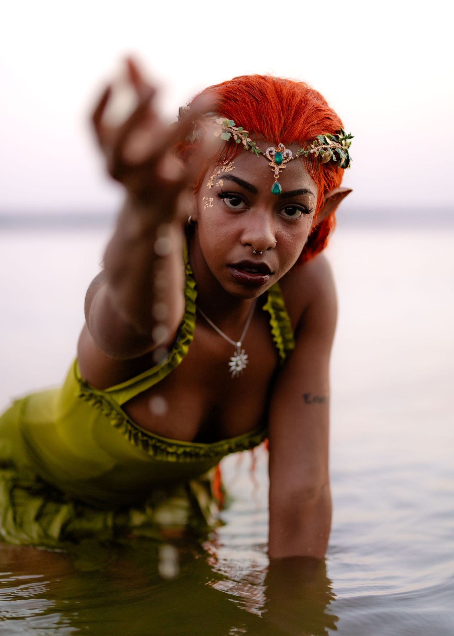 Artistic portrait of person with vibrant red hair and floral crown posing in water.