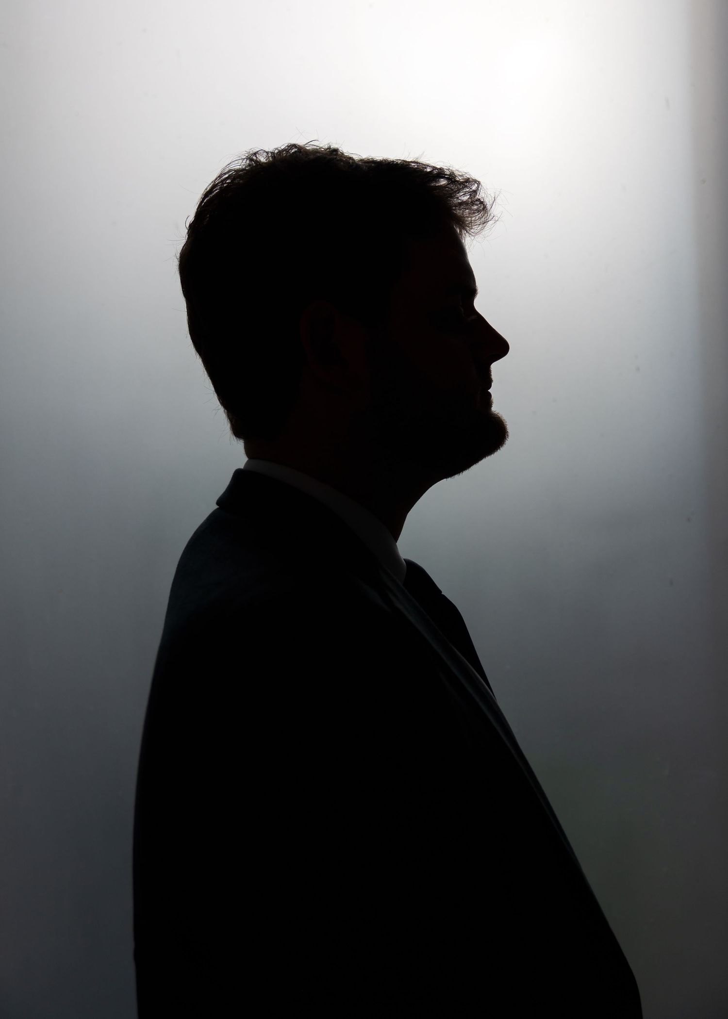 Dramatic silhouette profile of a man in a suit against a bright background in black and white.