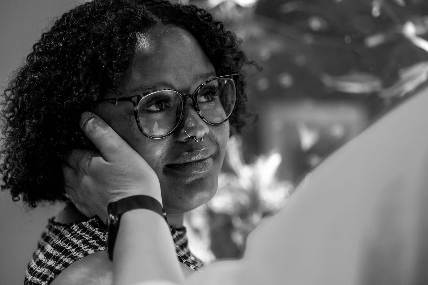 Black and white portrait of a woman with curly hair and glasses, resting her hand on her face thoughtfully.