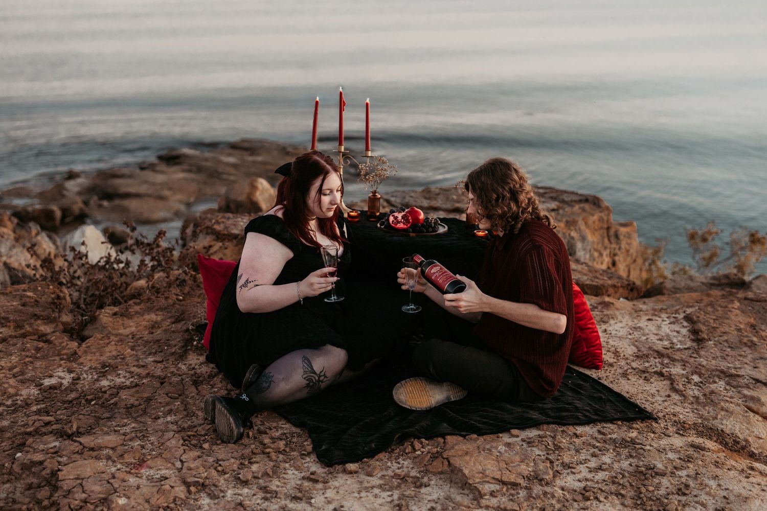 Romantic scene with red candles on a rocky coastal cliff at sunset.