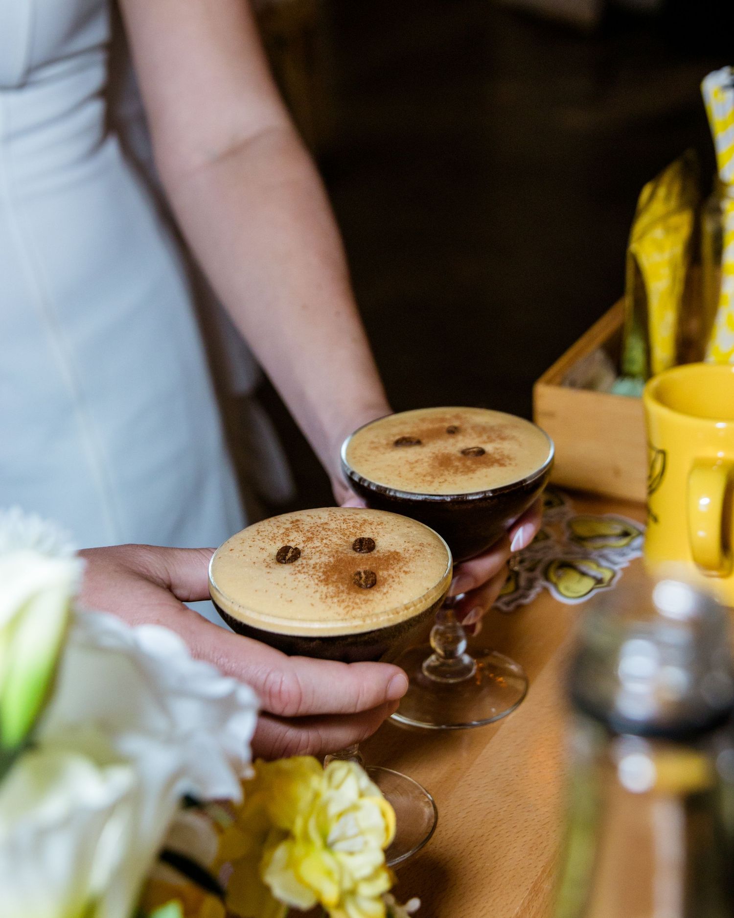 Close-up of hands pouring espresso martinis into vintage coupe glasses.