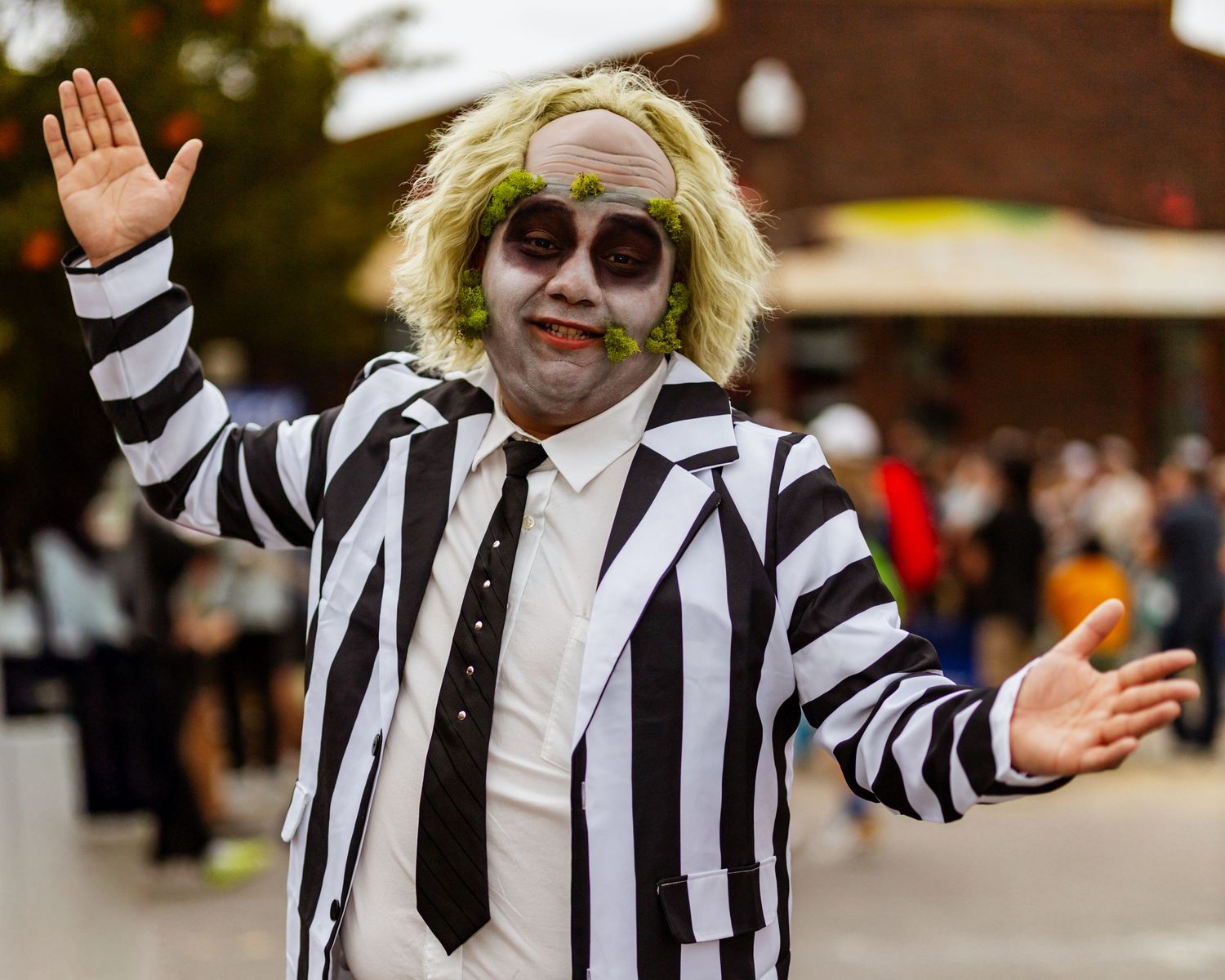 Person wearing black and white striped jacket and sunglasses gestures with hands in outdoor setting.