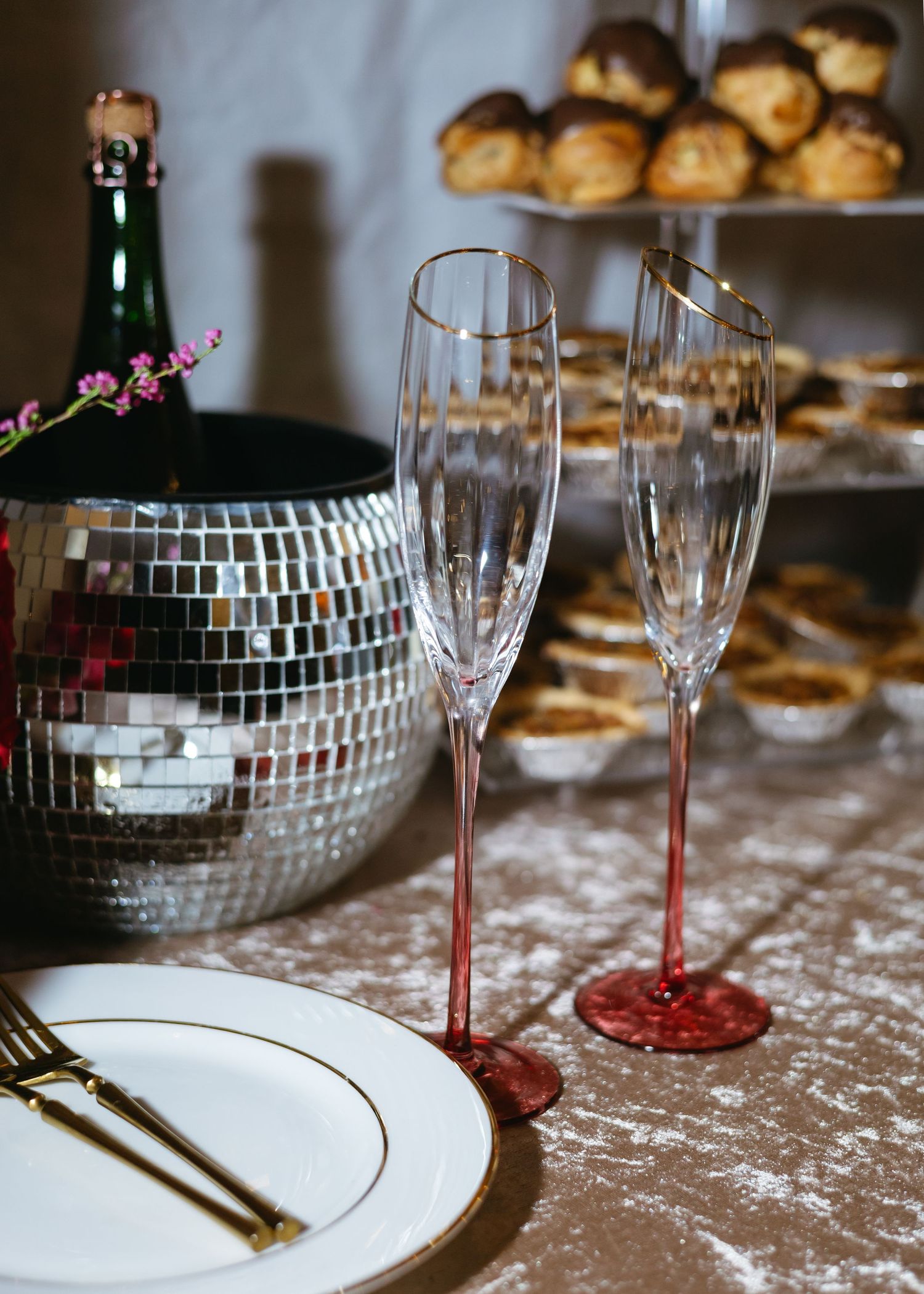 Elegant crystal champagne flutes with red stems beside a disco ball and champagne bottle at wedding reception.