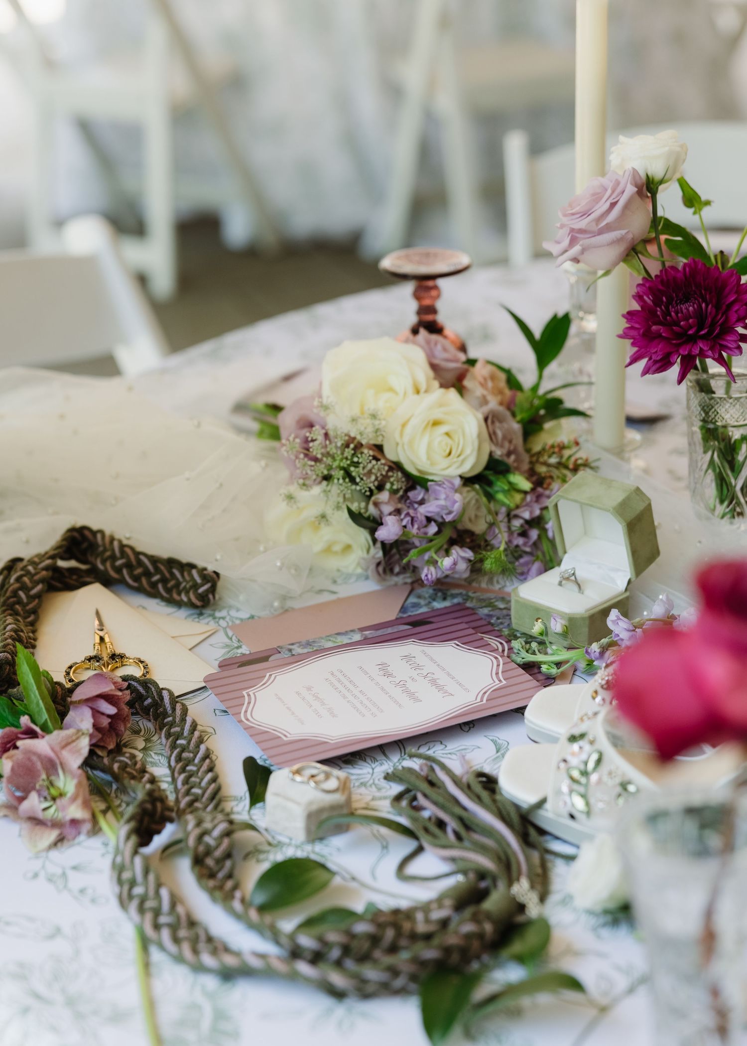 Elegant wedding tablescape with white and purple floral centerpiece, taper candles, and decorative menu cards on lace tablecloth.