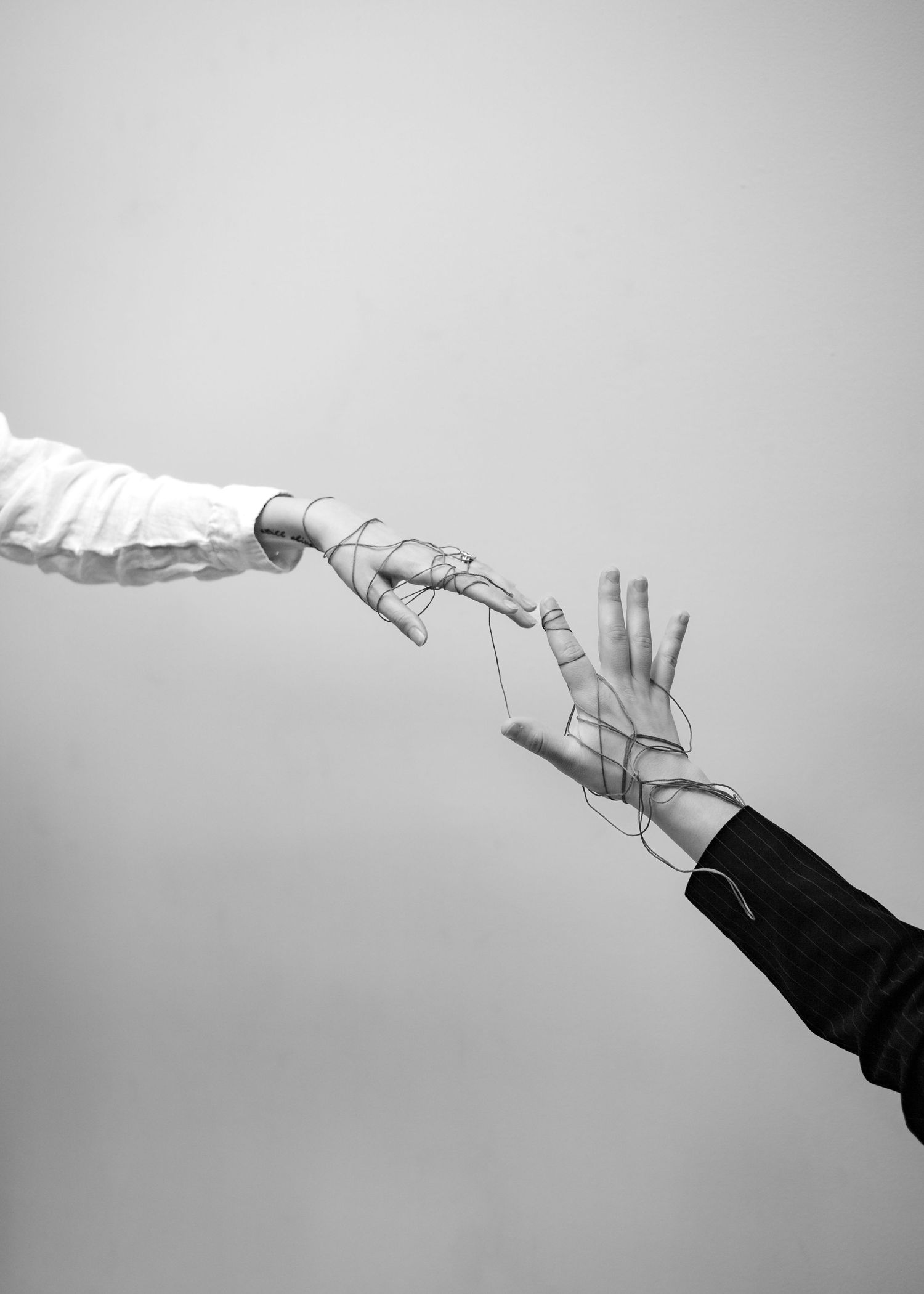Minimalist black and white photography of hands reaching with string against light background.