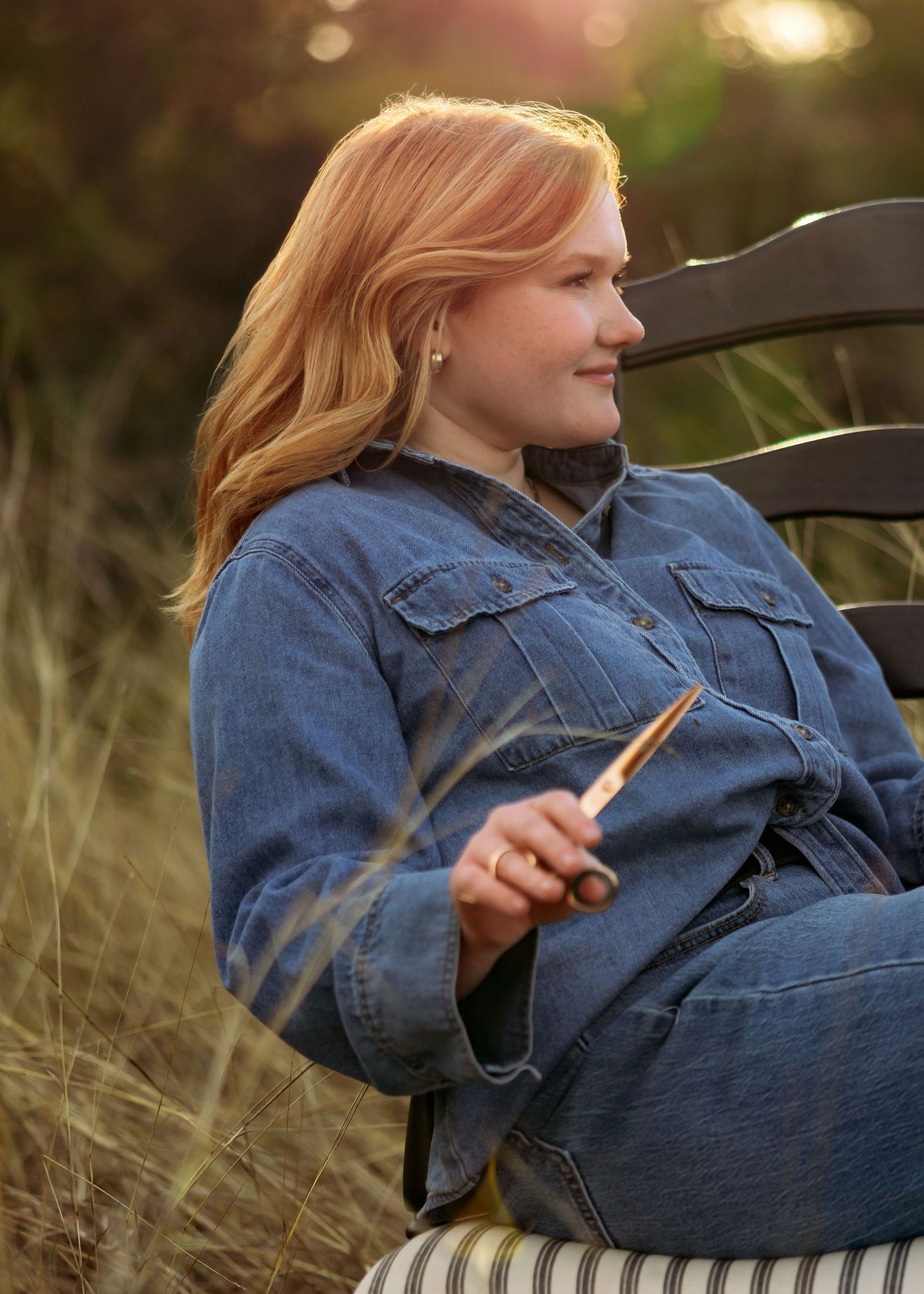 Someone relaxing in tall grass wearing a denim jacket while holding wooden items.