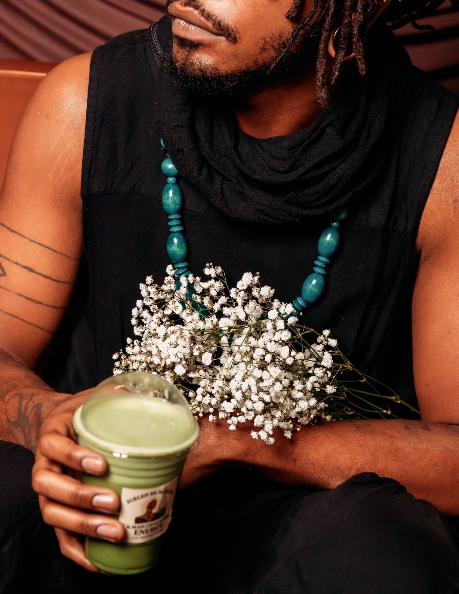 Hands holding a green drink with baby's breath flowers against a dark background.
