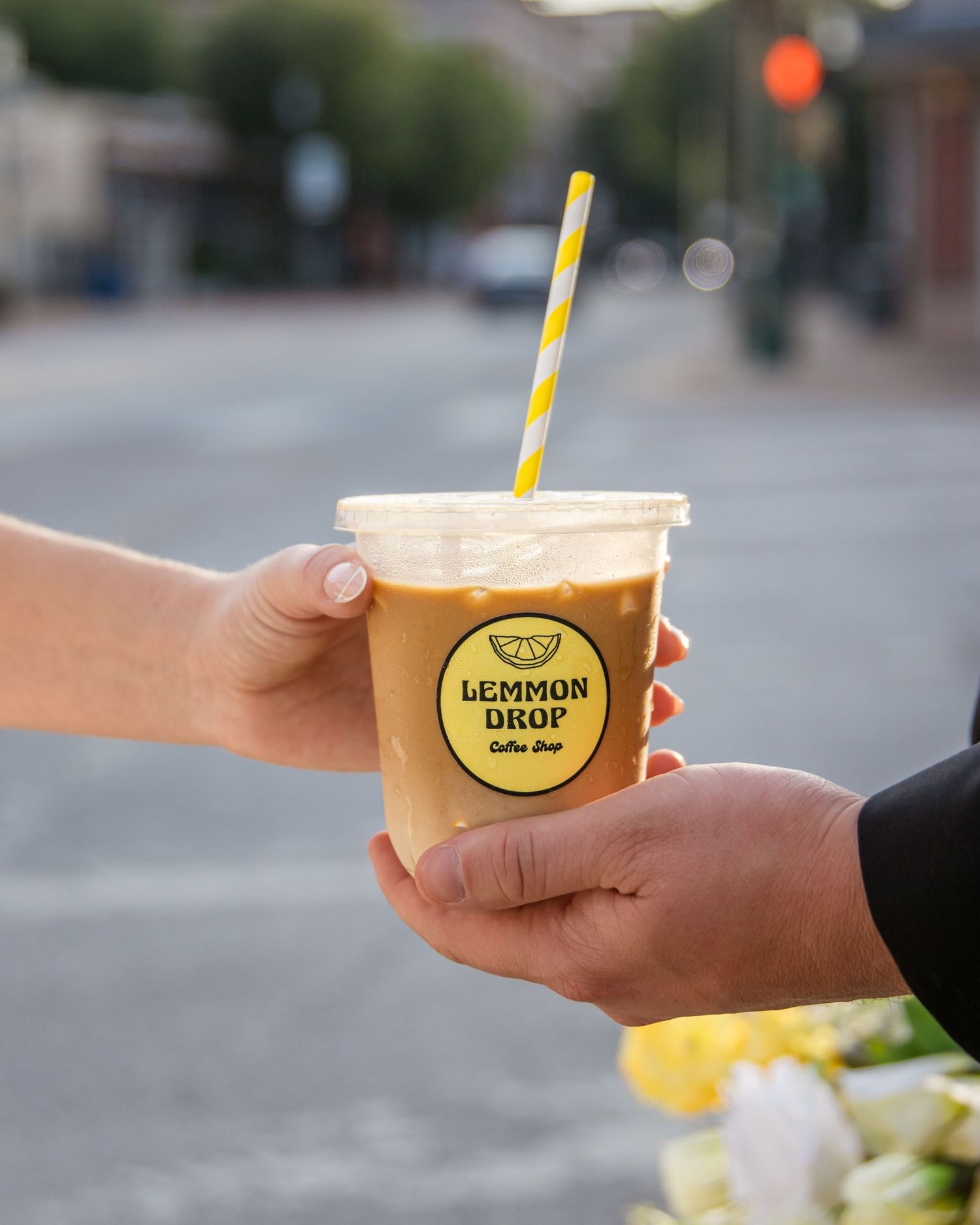 Yellow branded coffee cups being passed between hands outdoors.