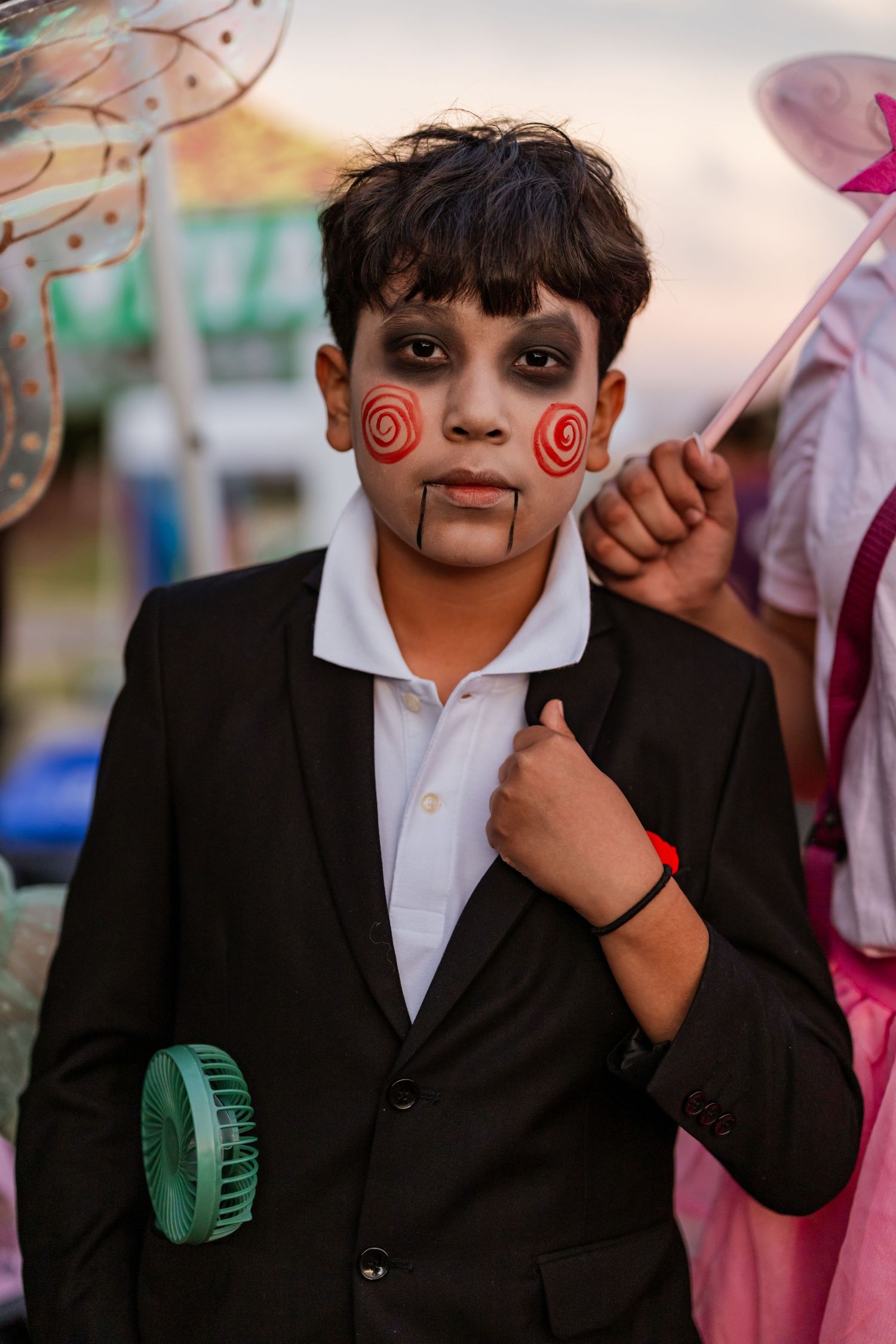 Child wearing formal suit with face painted in dramatic black and white spiral design at Halloween event.