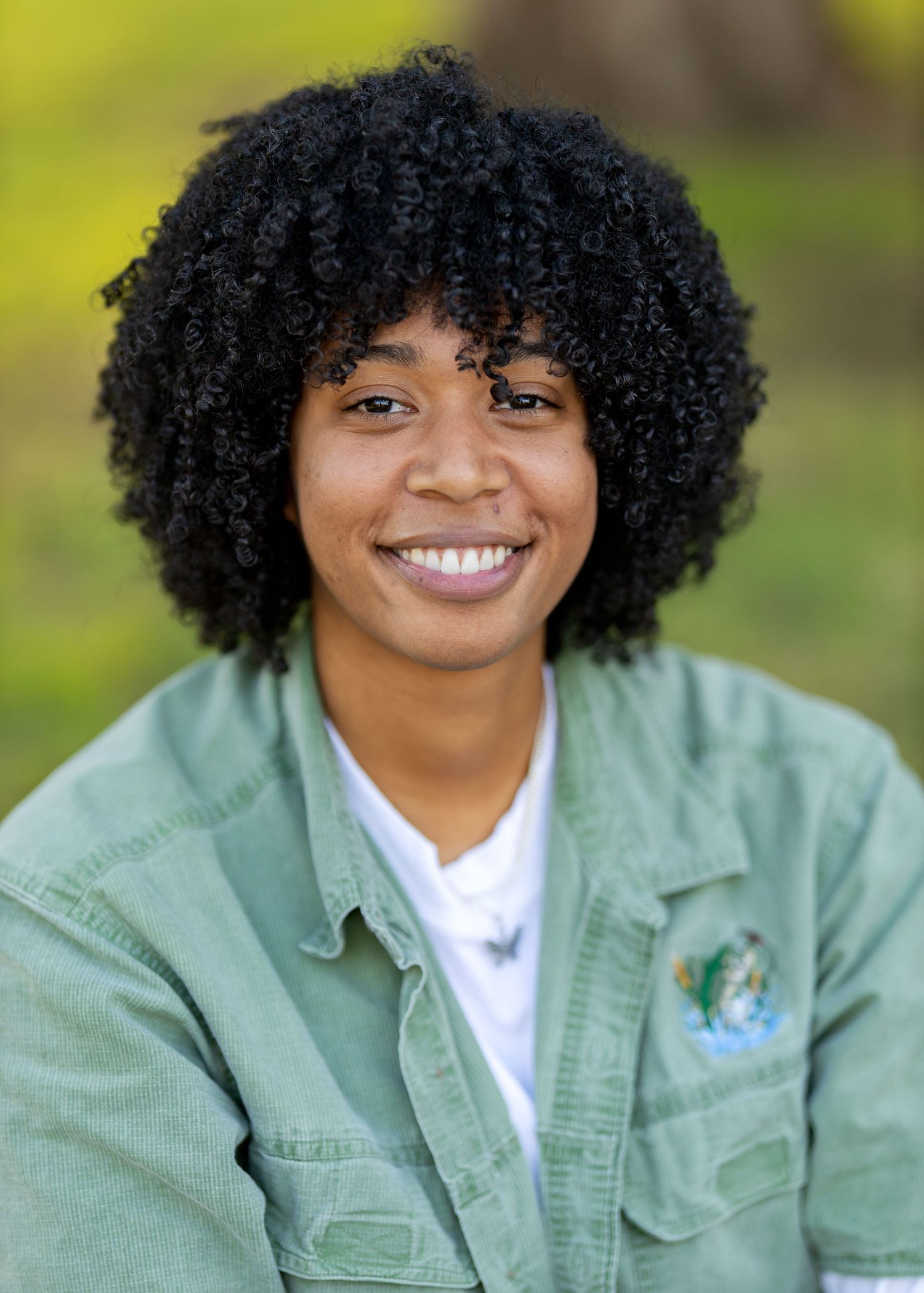 Person in mint green jacket and white shirt sitting casually outdoors.