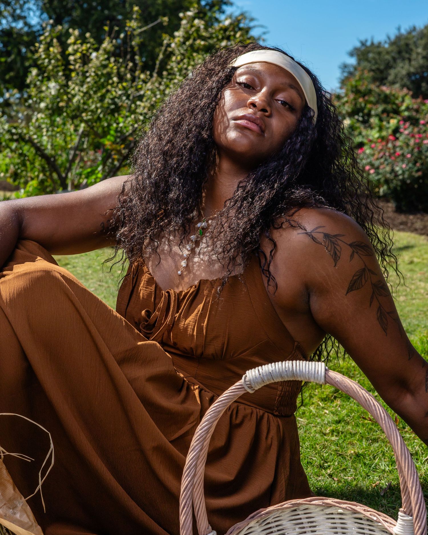 A person in a brown dress relaxes outdoors with a woven basket on a sunny day.