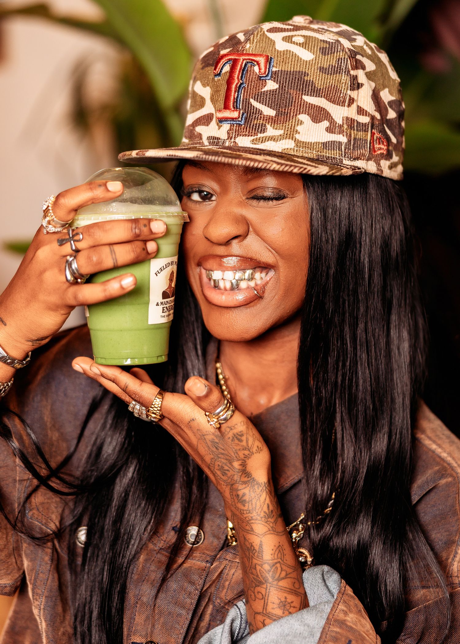 Person in camo hat drinking green matcha beverage.