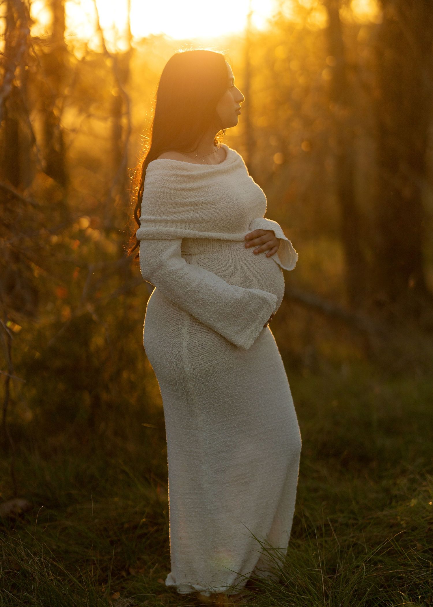 Figure wrapped in white fabric standing in golden sunlight among trees at sunset.