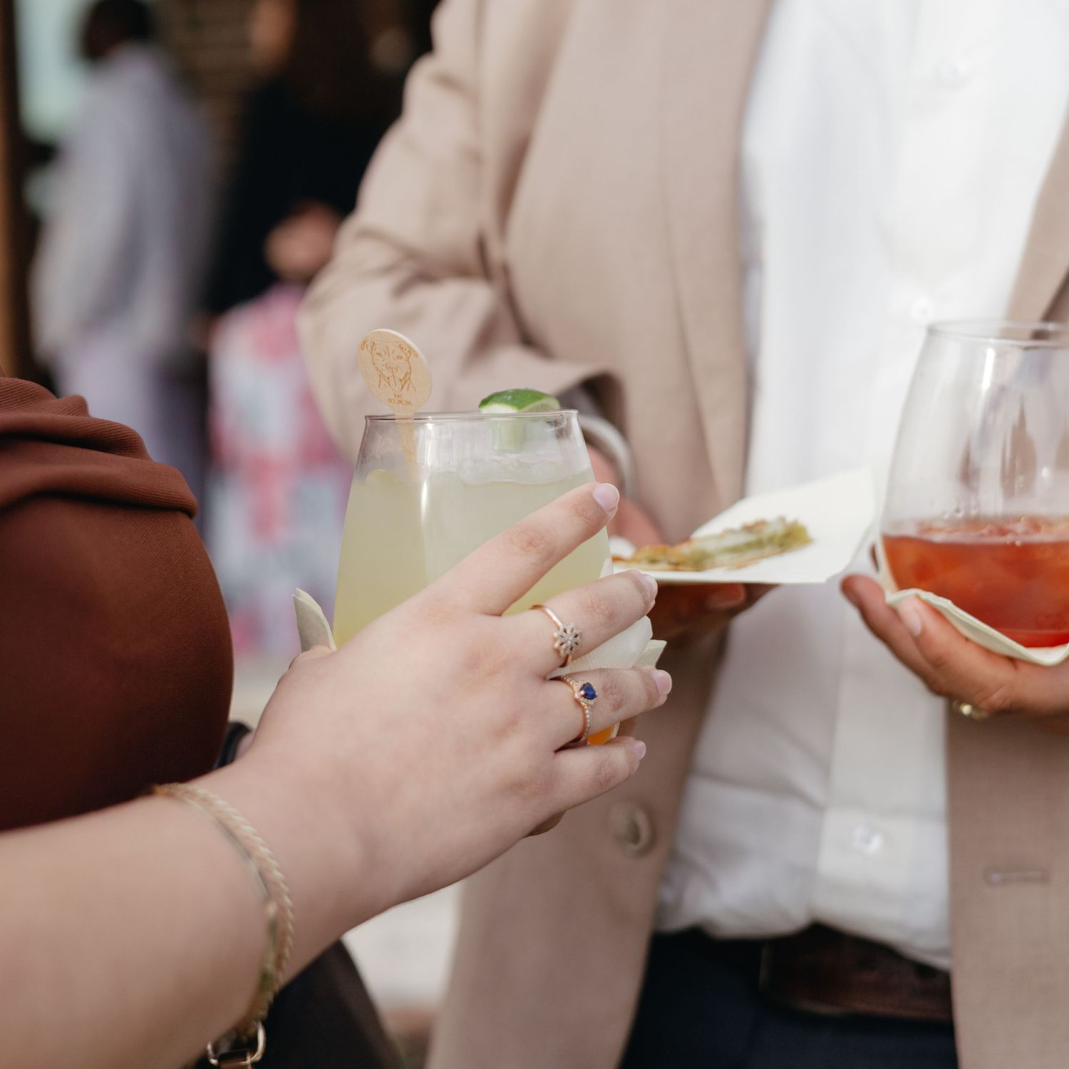 Two guests holding cocktails and appetizers at an elegant social gathering or cocktail party event.