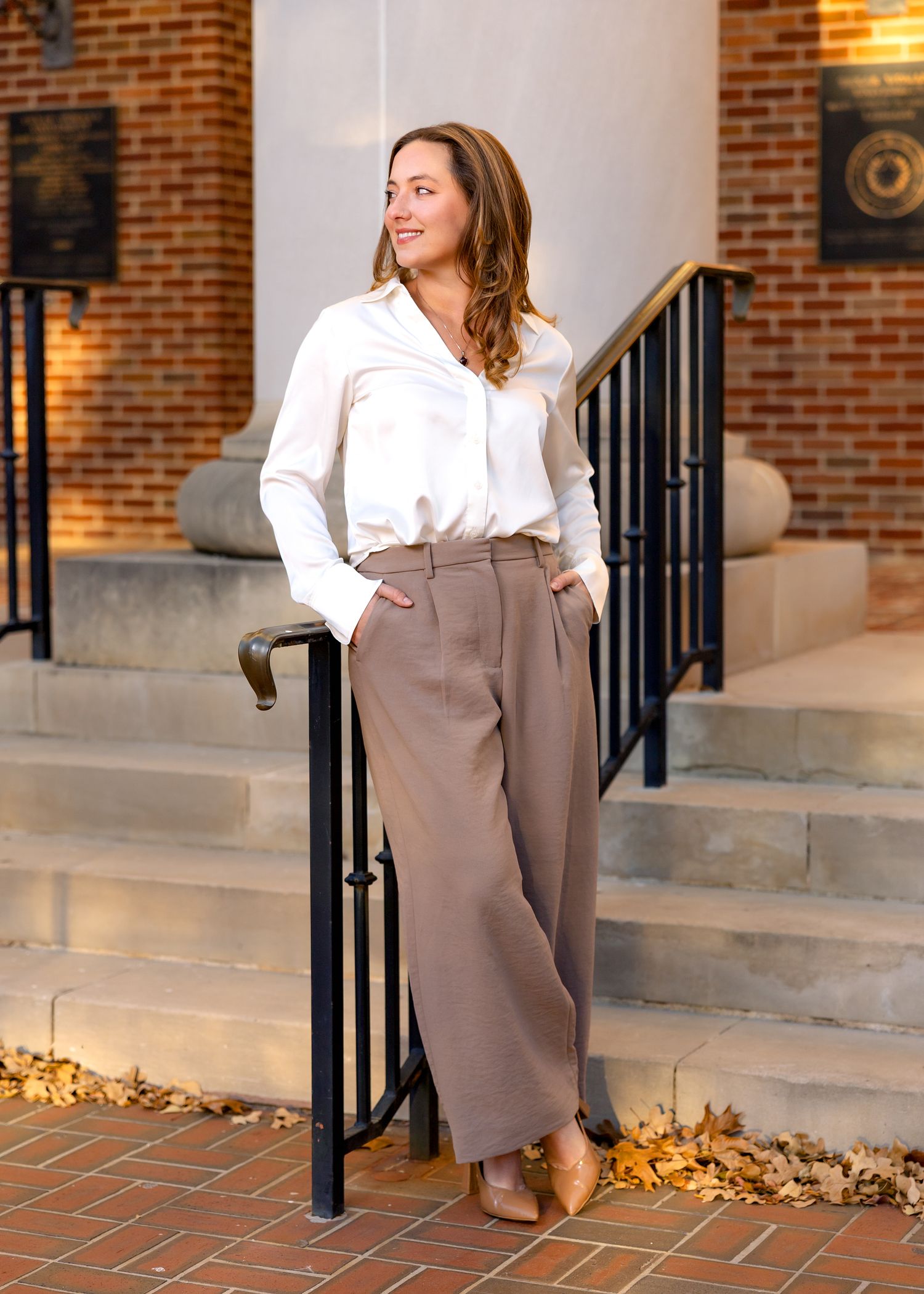 Professional standing portrait in business attire on brick building steps with black railing.