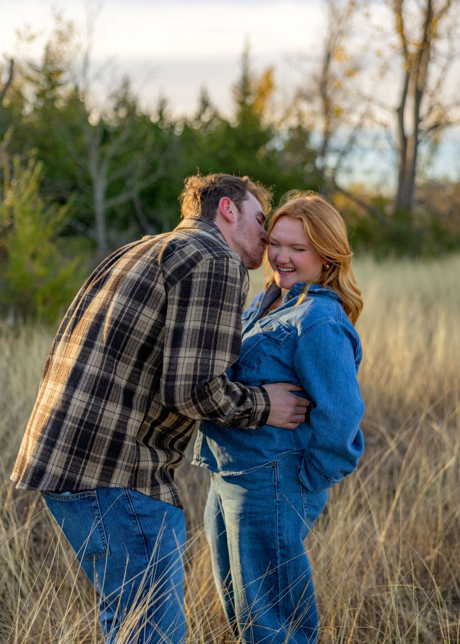 Couple sharing playful moments in a field with golden sunset light.