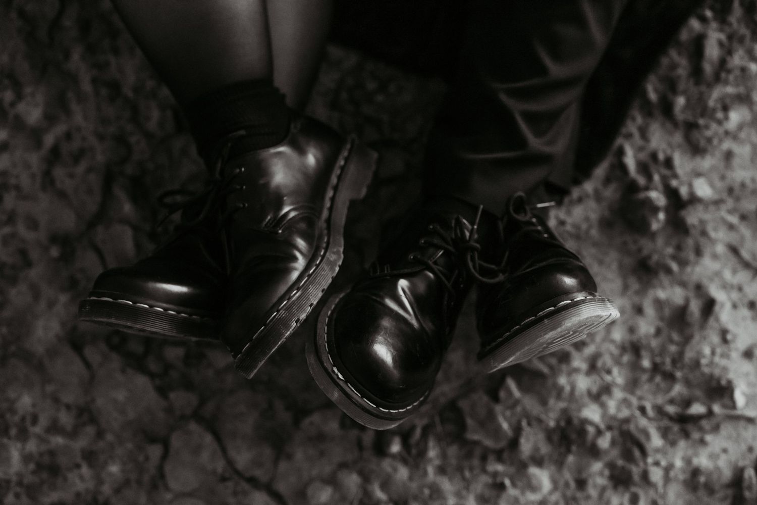 Dark moody photograph of black boots on textured rocky ground.
