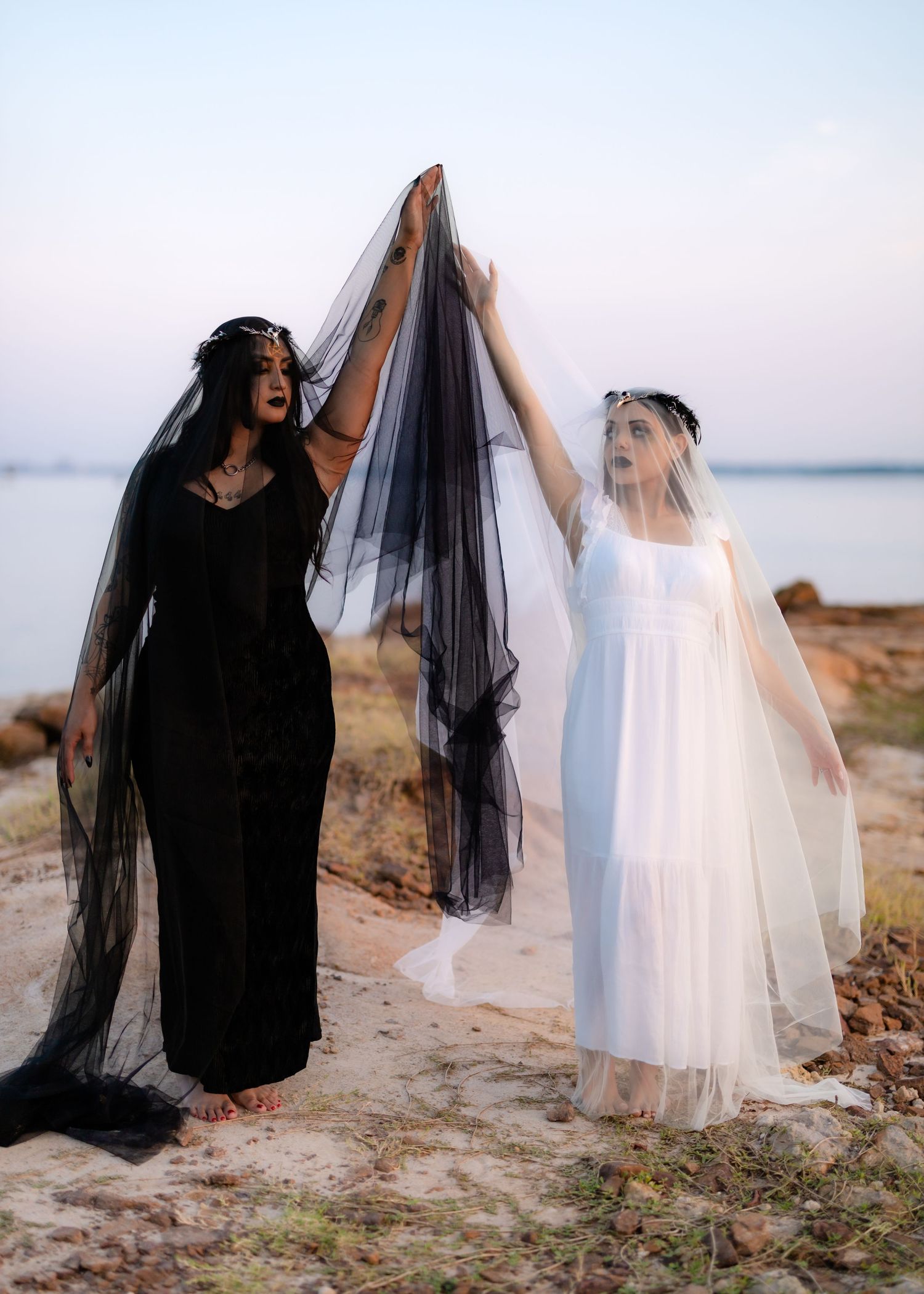 Two figures in contrasting black and white outfits dance playfully on a beach in an artistic photo series.